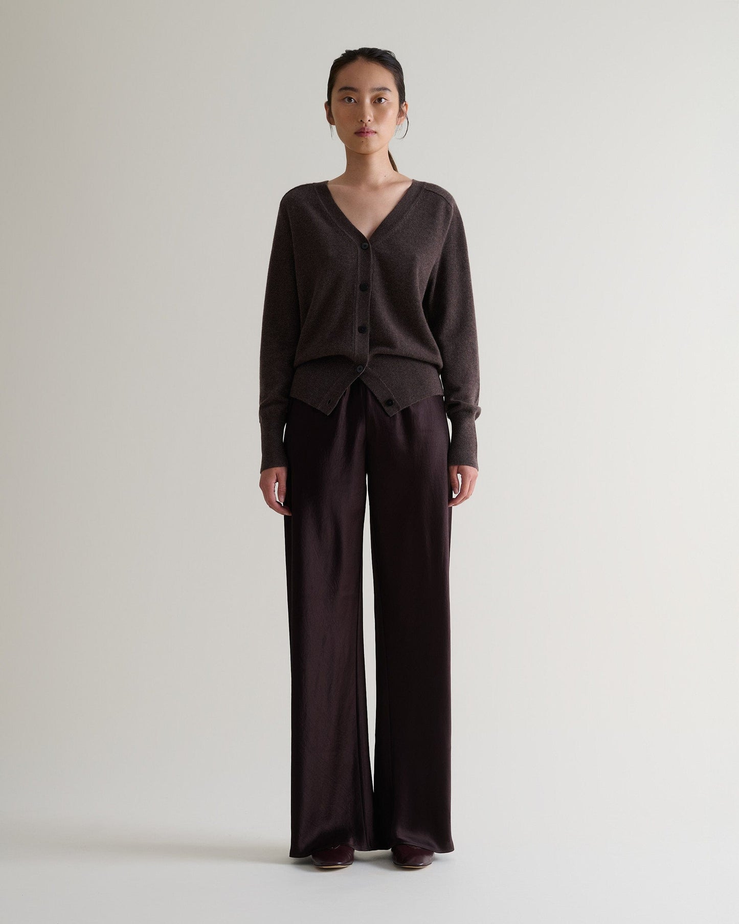 Image 3 of 6 showing woman wearing Rise & Fall's chocolate fine cashmere blouson cardigan with silk brown trousers.