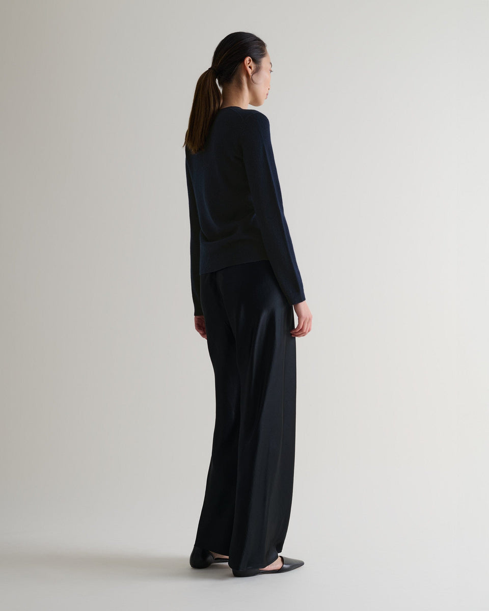 Image 3 of 6 showing side view of a woman wearing Rise & Fall's indigo cashmere merino henley jumper with black silk trousers. 