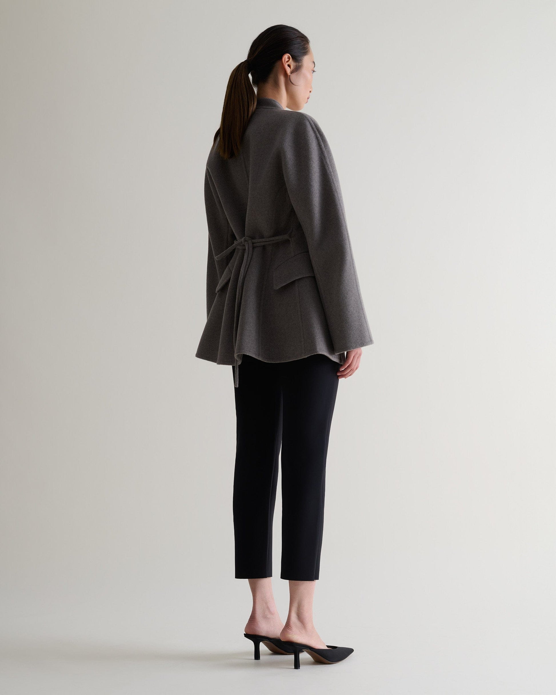 Image 3 of 7 showing woman wearing Rise & Fall's fawn cashmere wool double faced sculptural jacket with black cropped trousers.