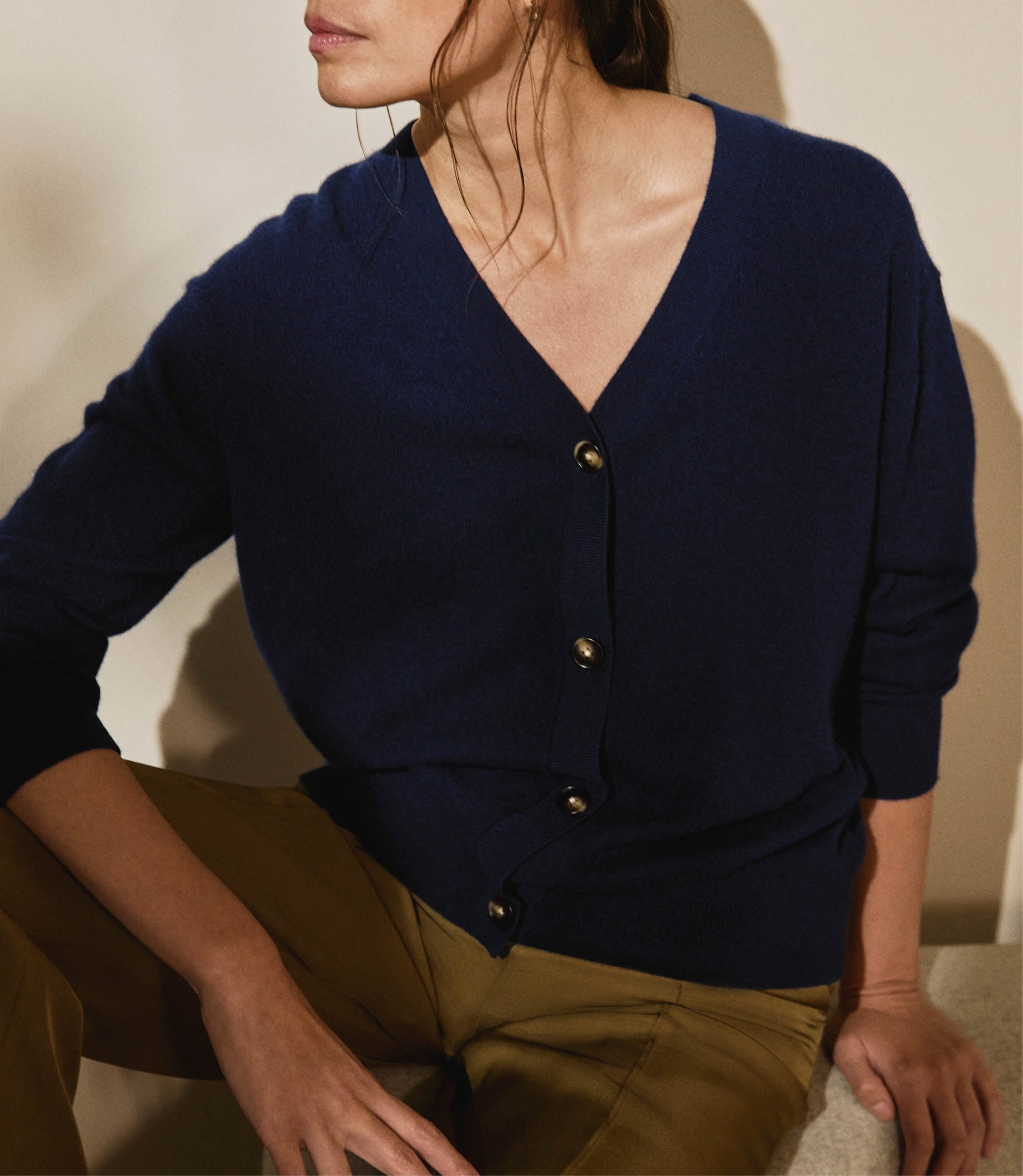 Image 4 of 4 showing woman wearing Rise & Fall's navy fine cashmere v-neck cardigan with olive trousers.