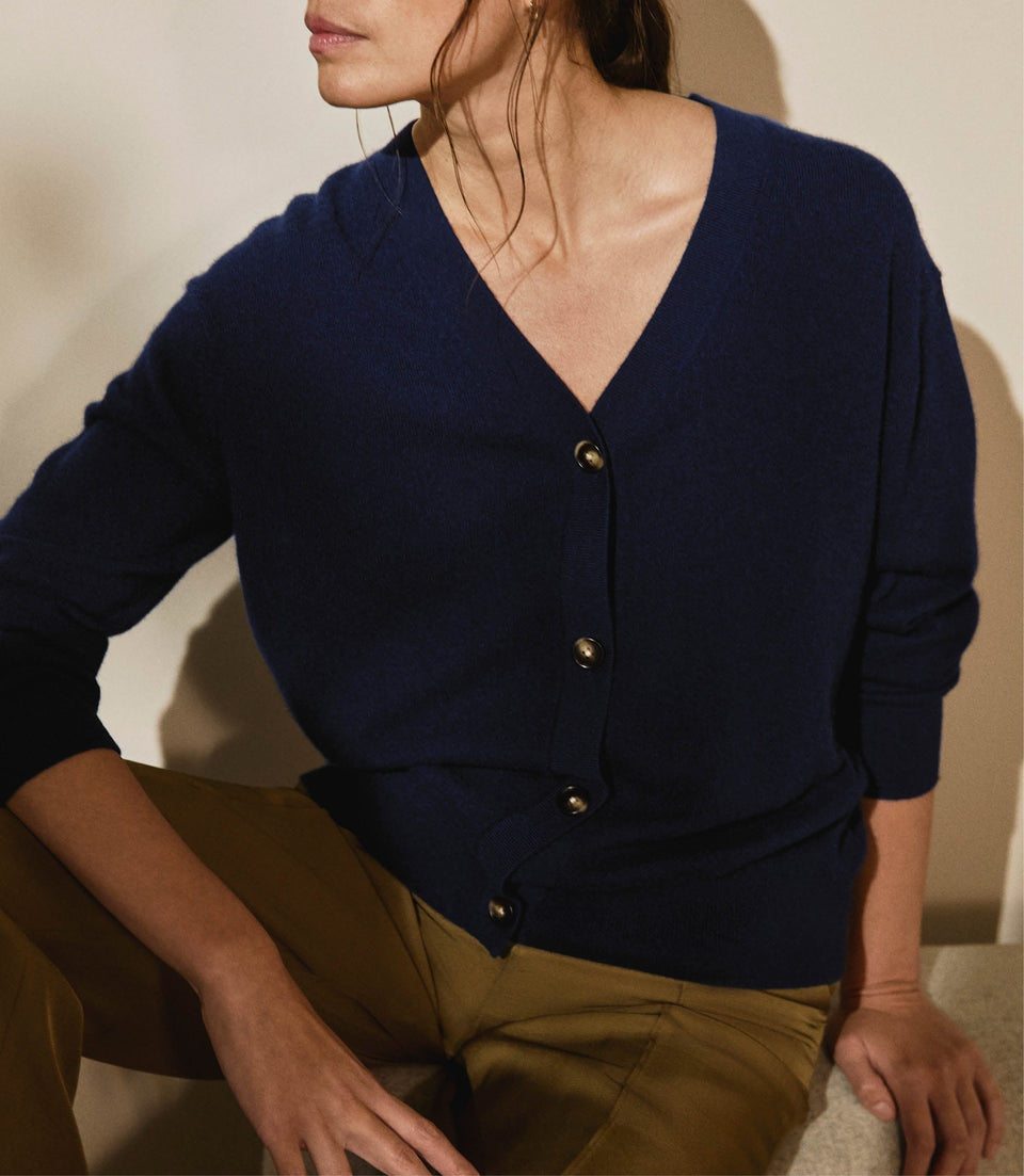 Image 4 of 4 showing woman wearing Rise & Fall's navy fine cashmere v-neck cardigan with olive trousers.