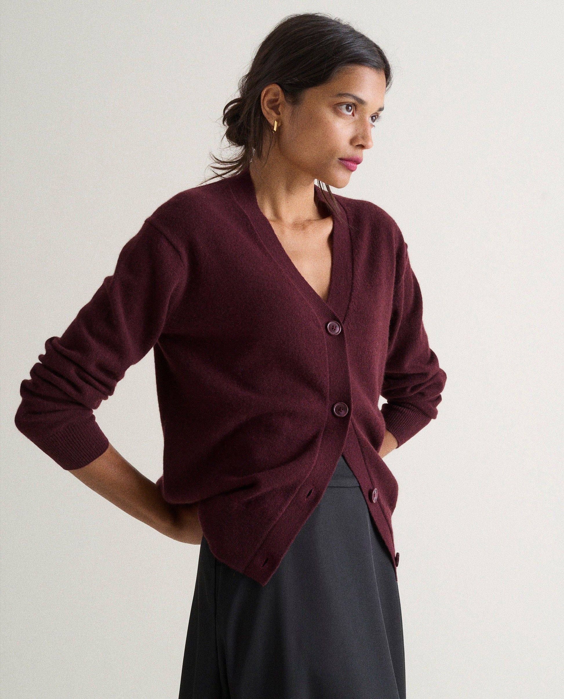 Image 4 of 4 showing side view of woman wearing Rise & Fall's oxblood fine cashmere v-neck cardigan with black skirt.