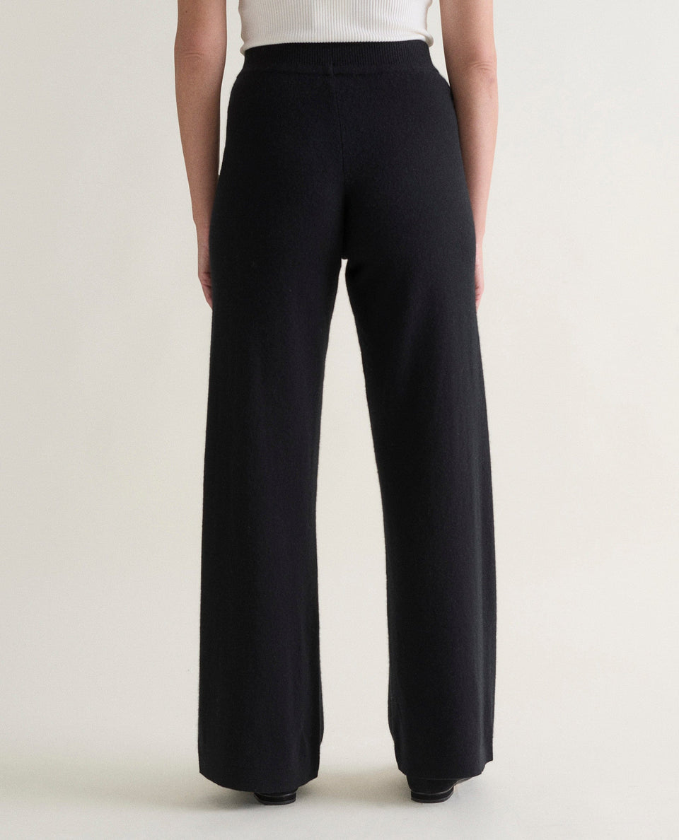 Image 4 of 4 showing back of woman wearing Rise & Fall's black fine cashmere wide-leg trousers with a white top.