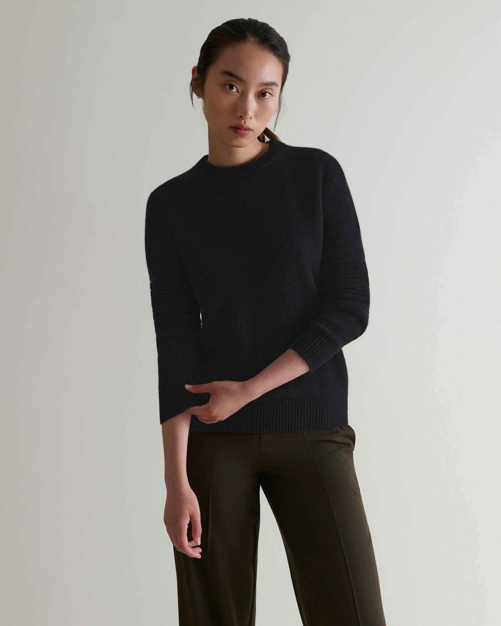 Image 4 of 4 showing woman wearing Rise & Fall's black mid-weight cashmere crew neck jumper with brown silk trousers.