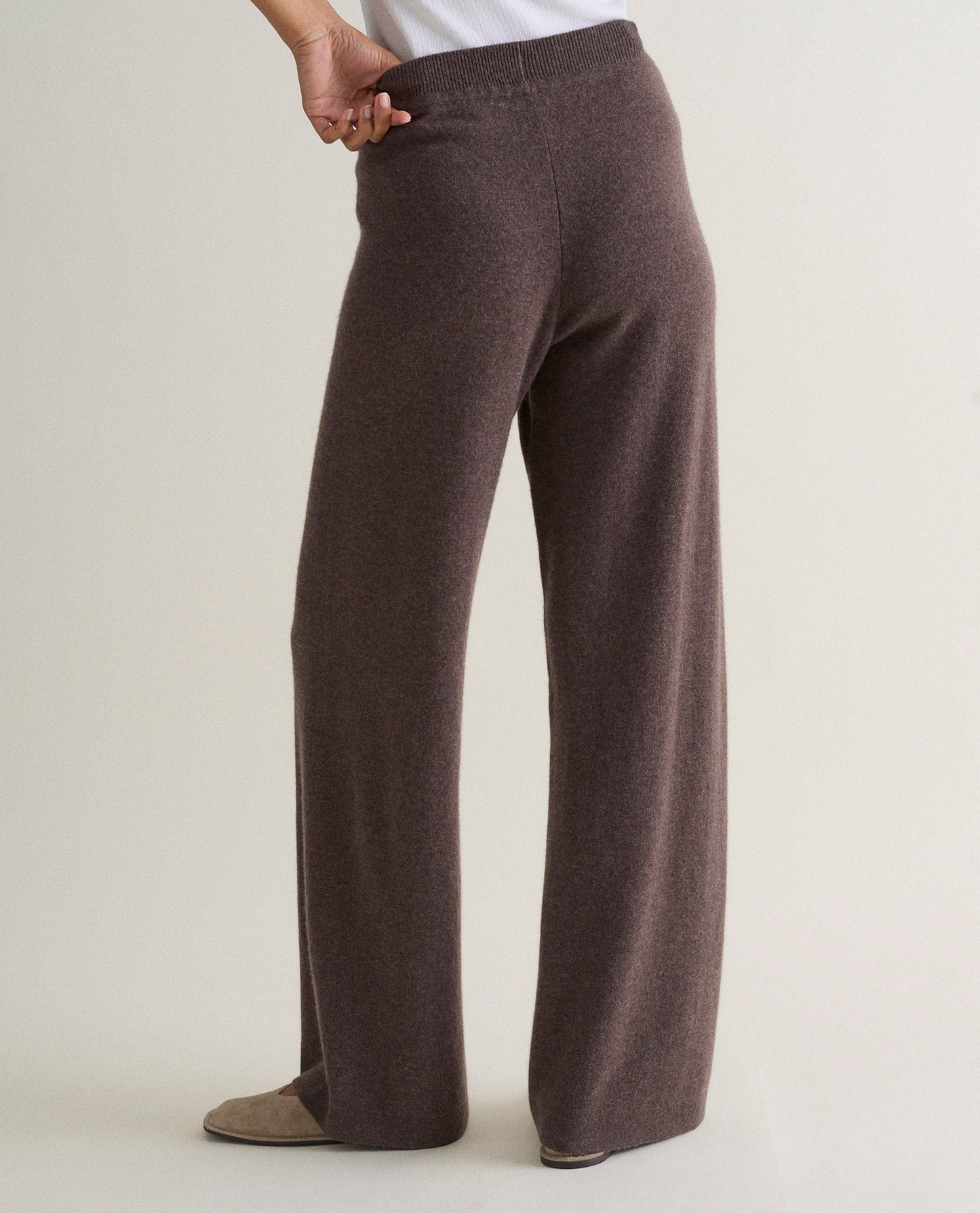 Image 4 of 4 showing the back of a woman wearing Rise & Fall's chocolate brown fine cashmere wide-leg trousers with a white top.