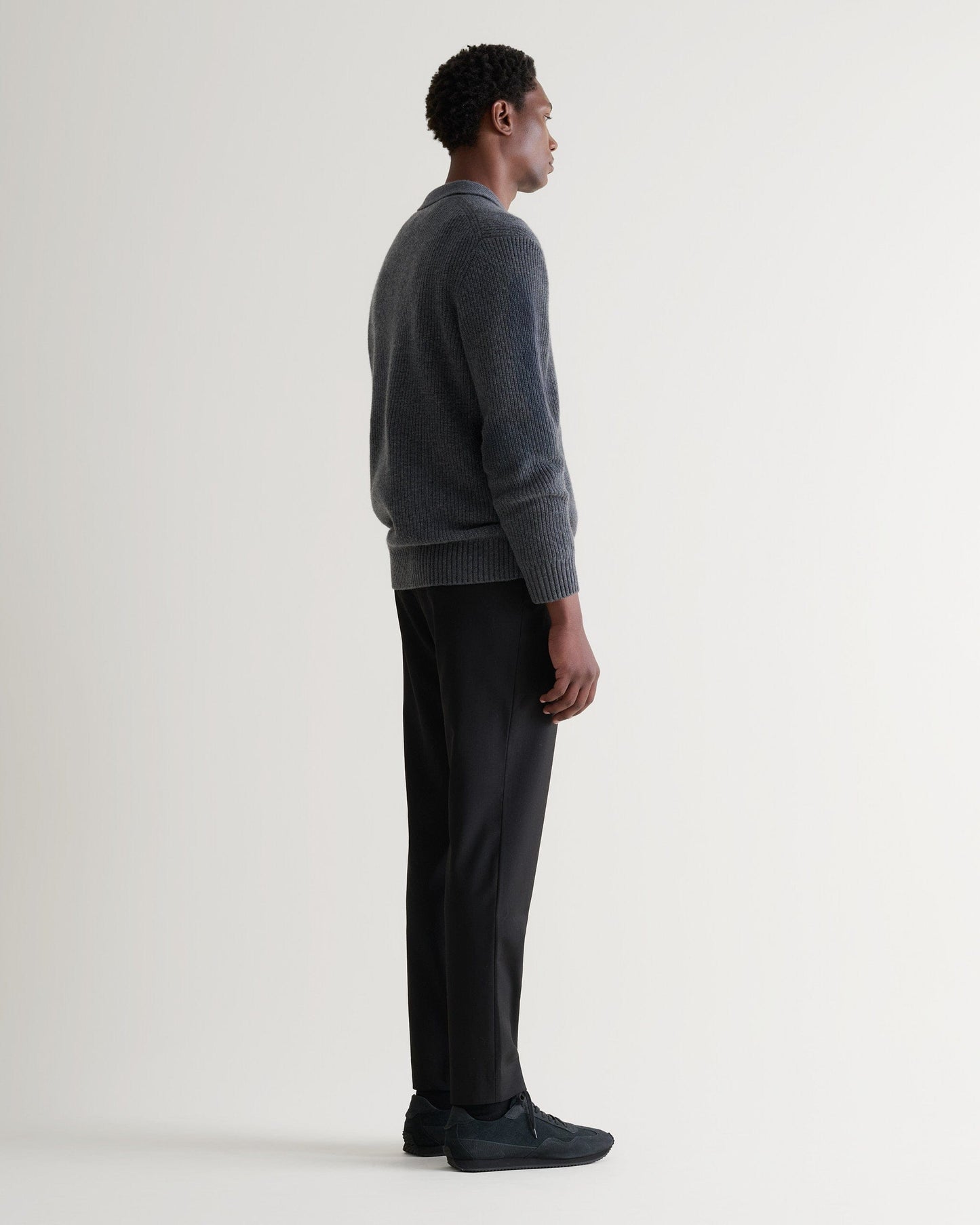 Image 4 of 5 showing side view of man wearing Rise & Fall's graphite cashmere merino fishe rman ribbed polo jumper with white T-Shirt and black trousers