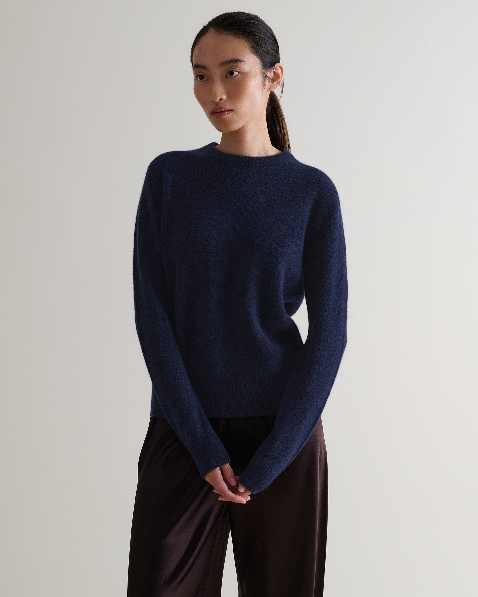 Image 4 of 5 showing woman wearing Rise & Fall's navy mid weight cashmere crew neck jumper with brown silk trousers.