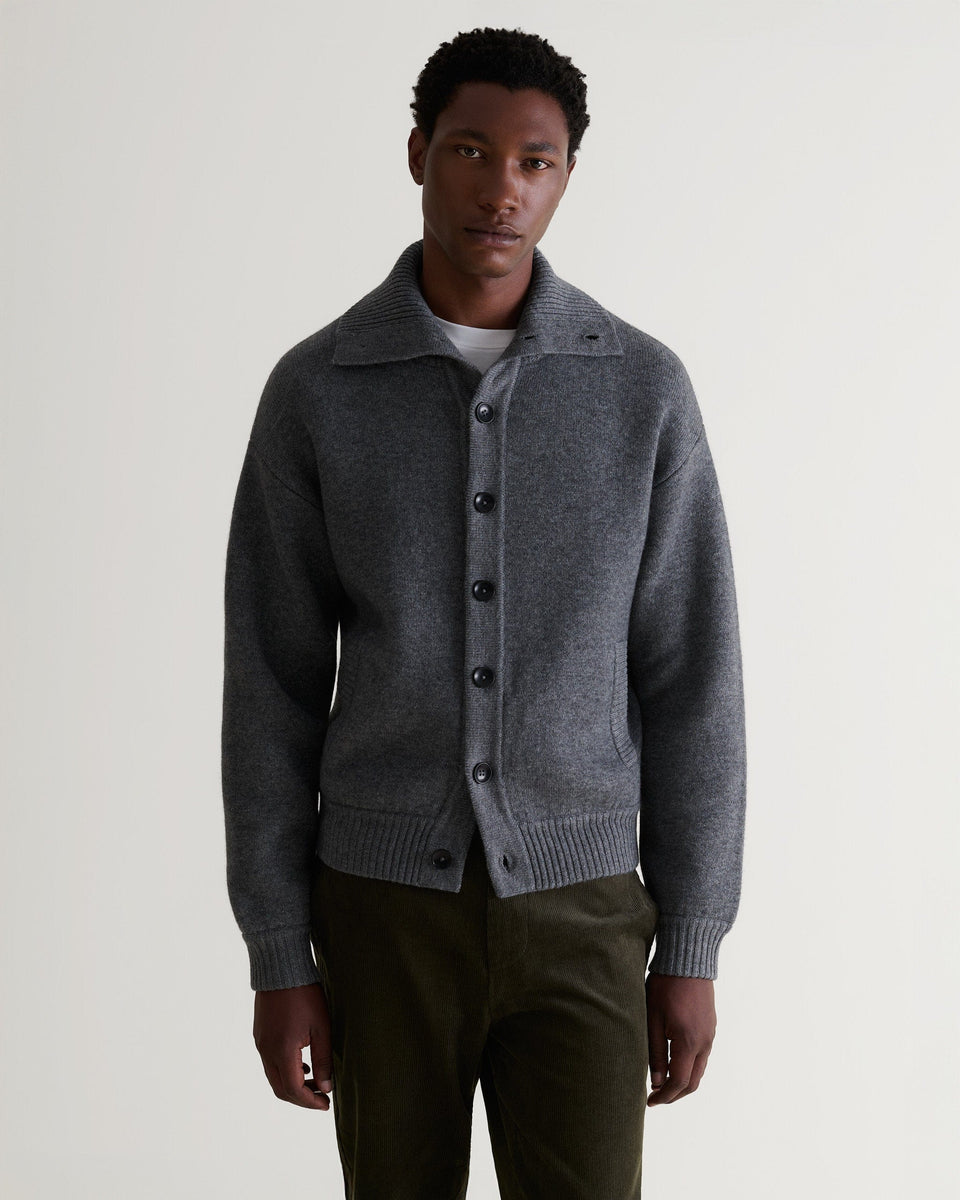 Image 4 of 6 showing man wearing Rise & Fall's dark grey cashmere merino buttoned knitted bomber with white T-shirt and green corduroy trousers.