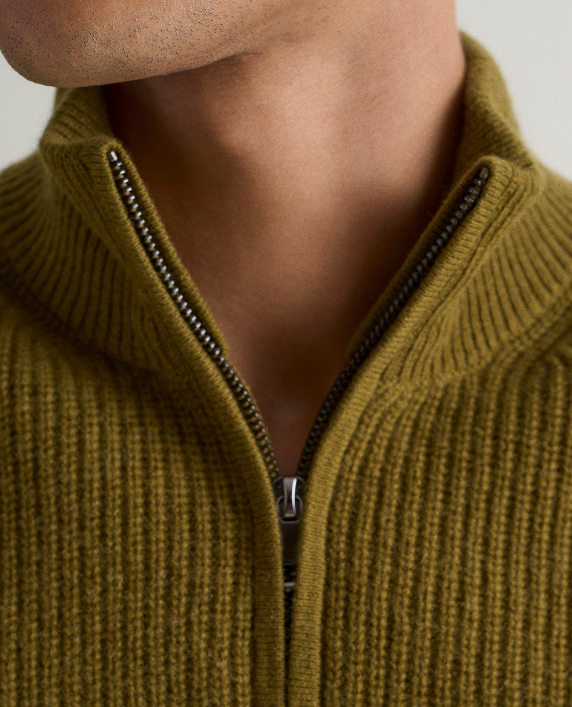 Image 4 of 6 showing close up of man wearing Rise & Fall's Cashmere Merino Fishermans Rib 1/4 Zip Jumper in olive green.