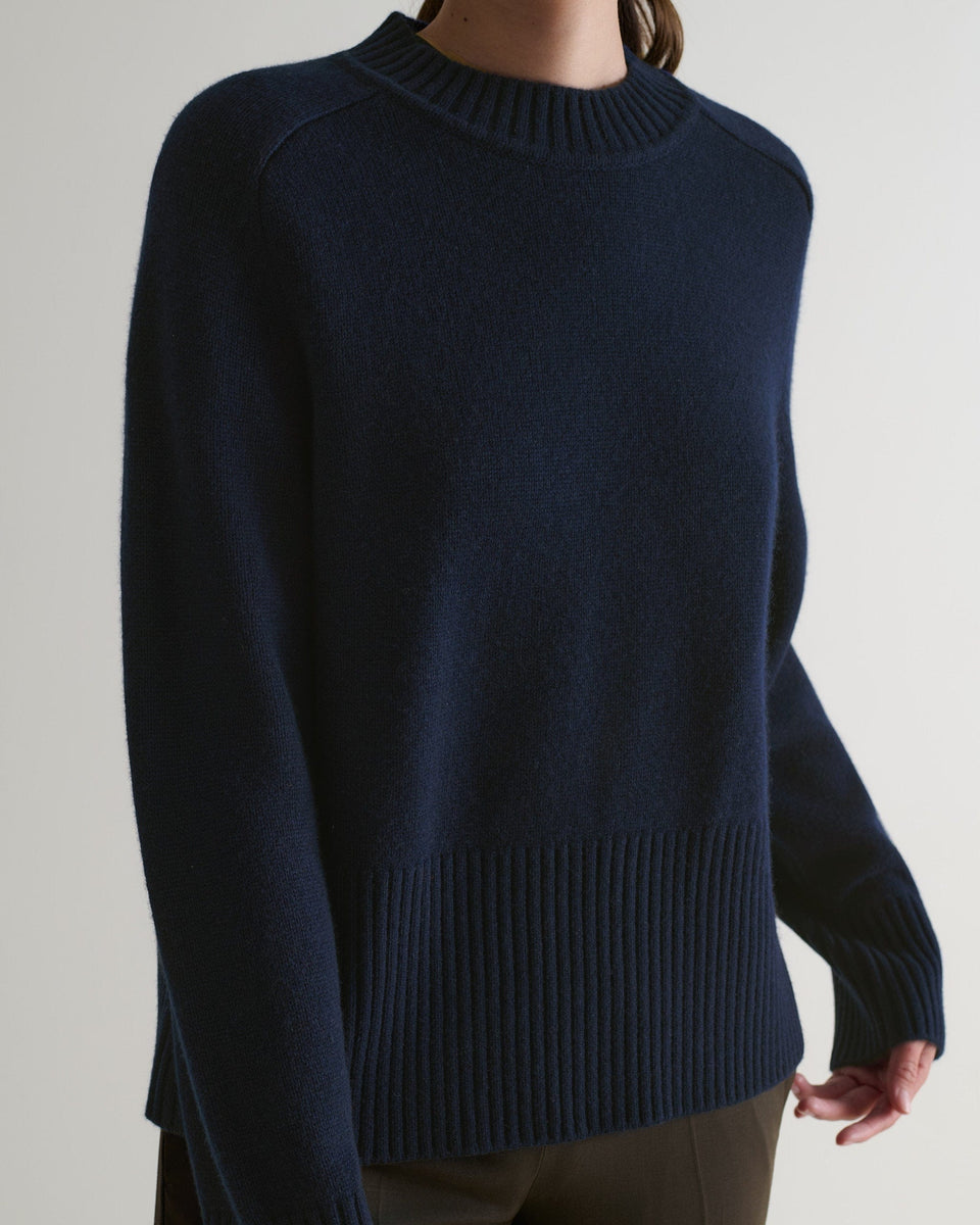 Image 4 of 6 showing close up of woman wearing Rise & Fall indigo cashmere merino saddle sleeve crew with brown trousers.