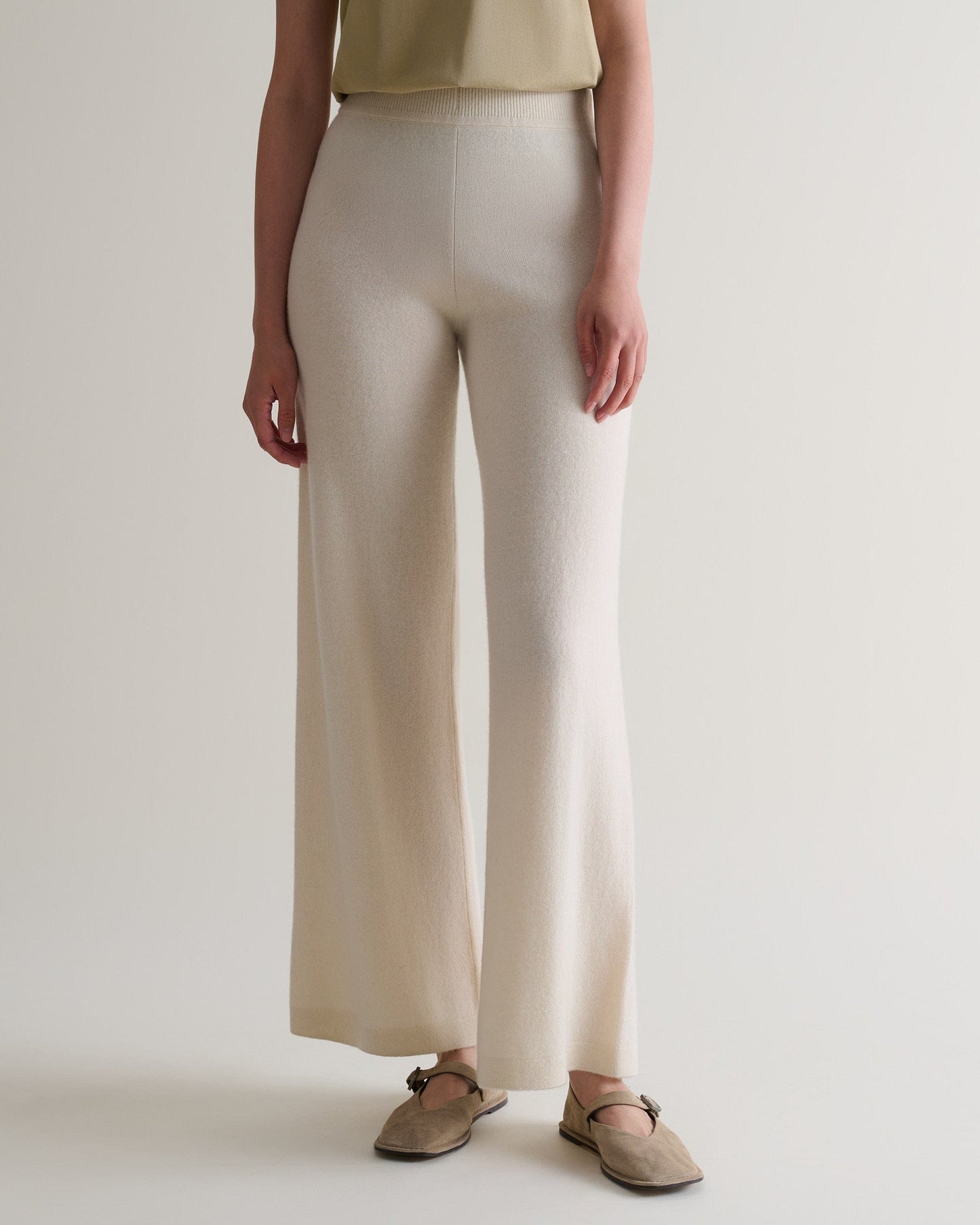 Image 4 of 6 showing close up of woman wearing Rise & Fall's cream fine cashmere wide-leg trousers with beige t-shirt and shoes.