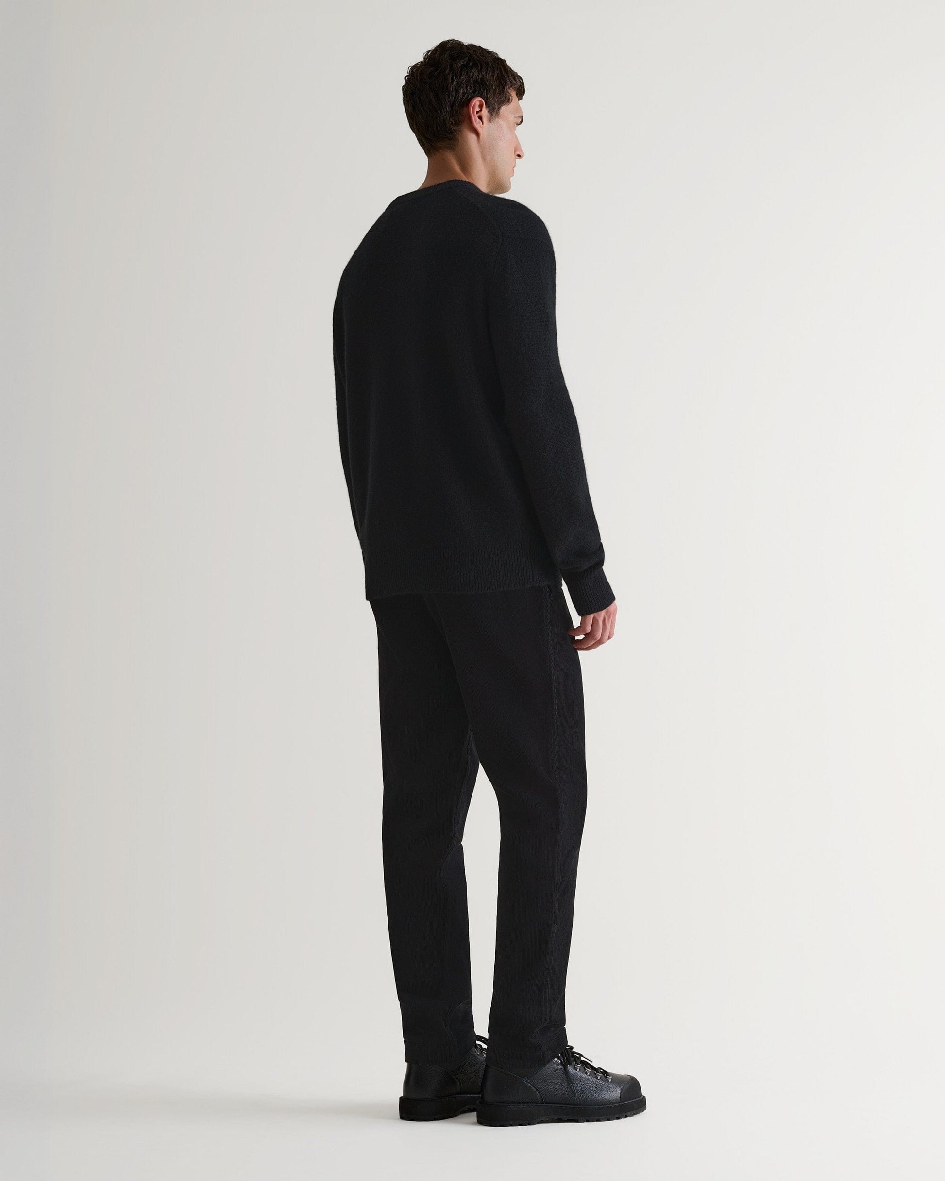 Image 4 of 7 showing back of man wearing Rise & Fall's Finest Cashmere Mid-Weight Crew Neck Jumper in black with tailored black trousers.