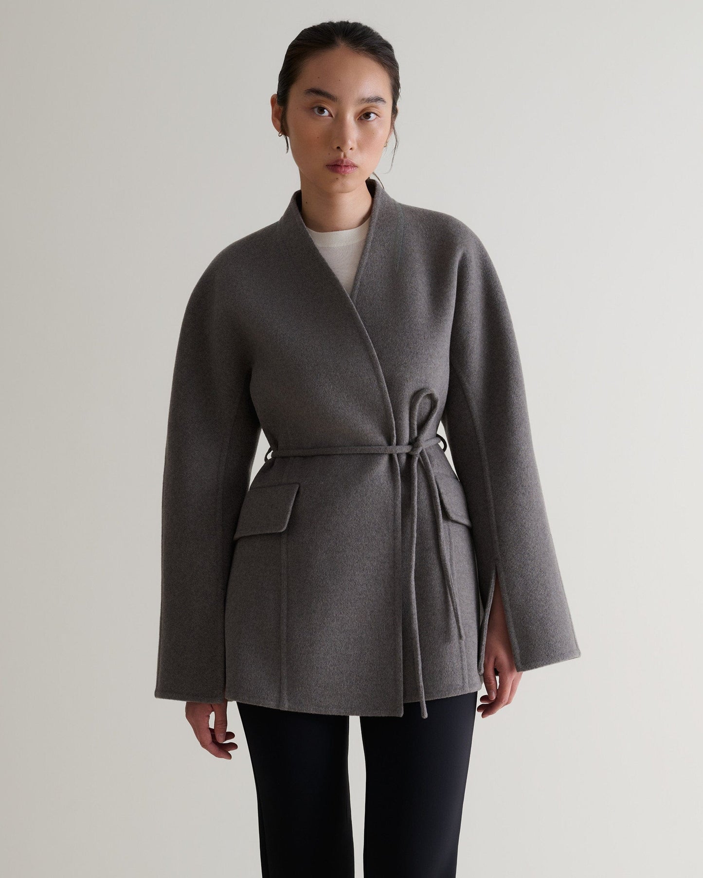 Image 4 of 7 showing woman wearing Rise & Fall's fawn cashmere wool double faced sculptural jacket with white t-shirt and black trousers.