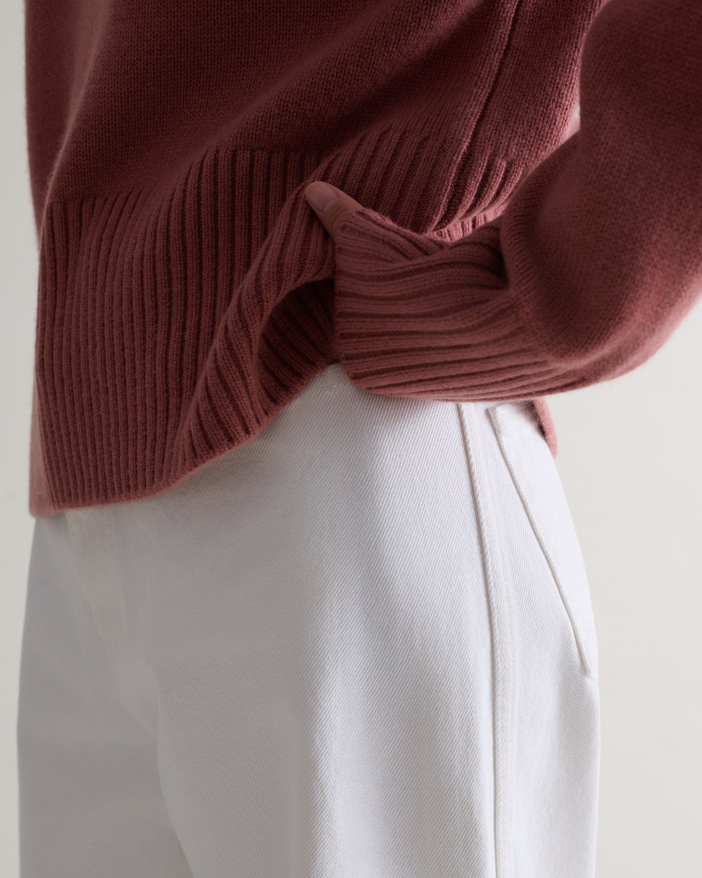 Image 5 of 5 showing a close up of Rise & Fall's pink clay cashmere merino saddle sleeve crew neck jumper with white jeans.