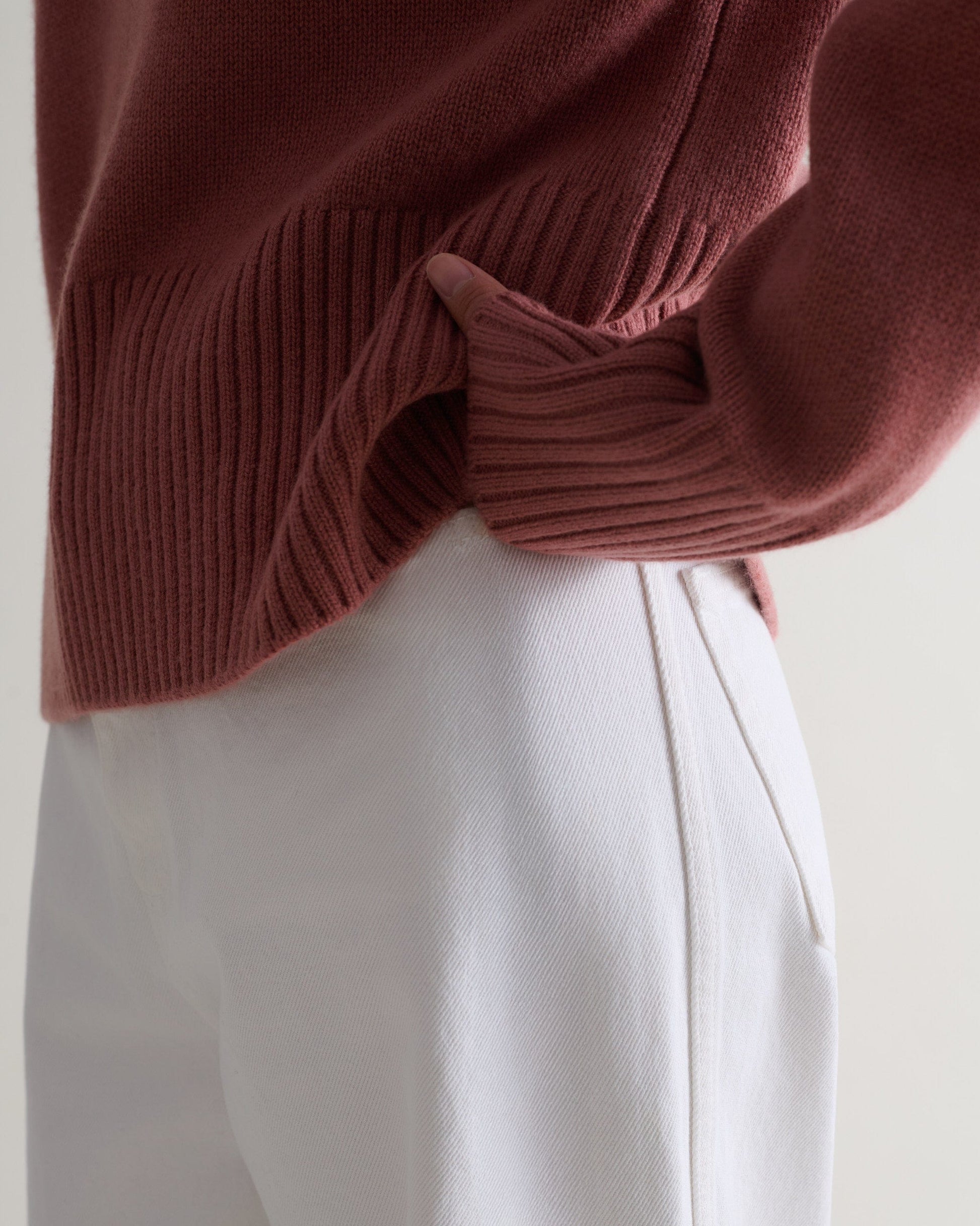 Image 5 of 5 showing a close up of Rise & Fall's pink clay cashmere merino saddle sleeve crew neck jumper with white jeans.