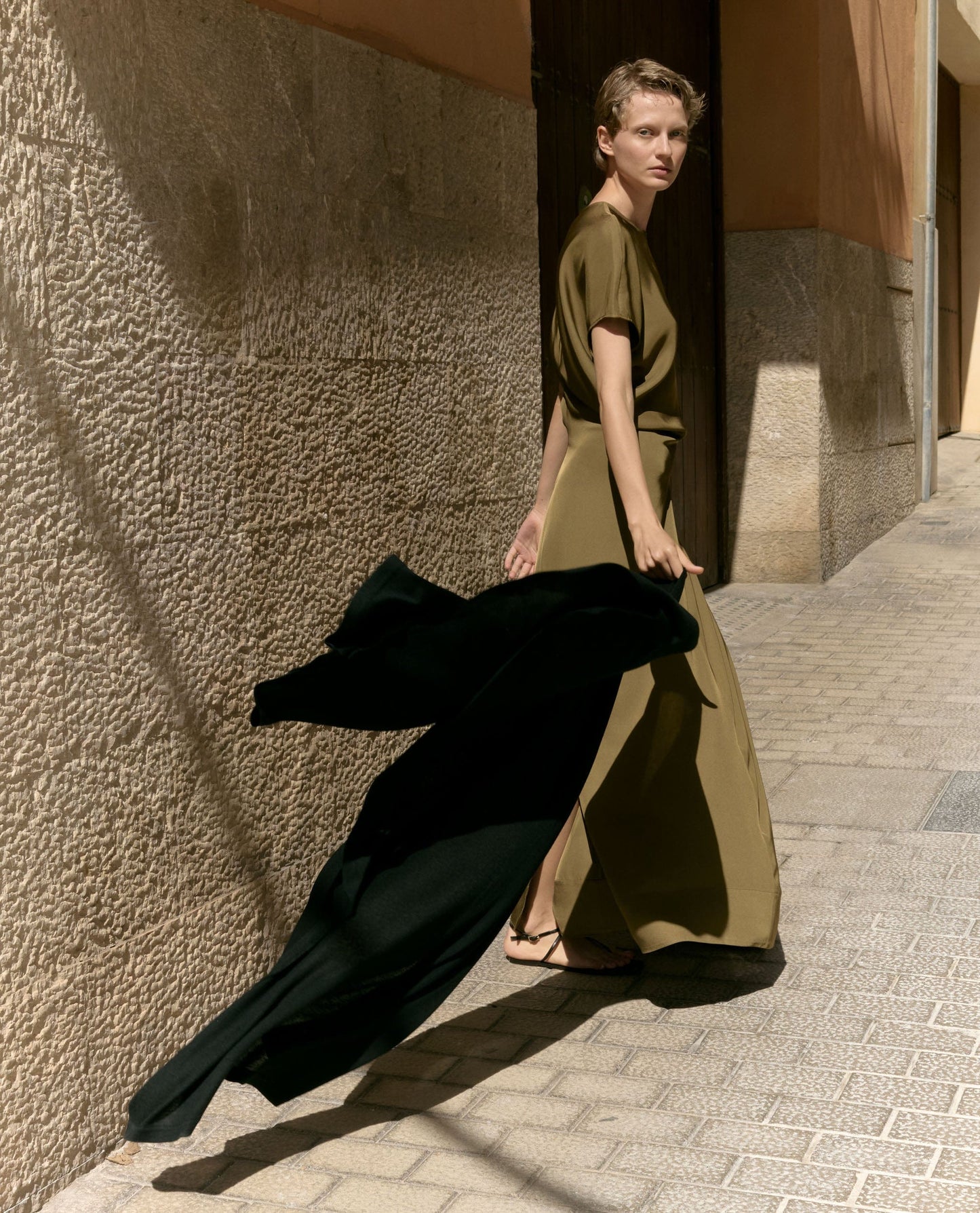 Image 5 of 5 showing woman holding Rise & Fall's black oversized cashmere scarf behind her as she walks.