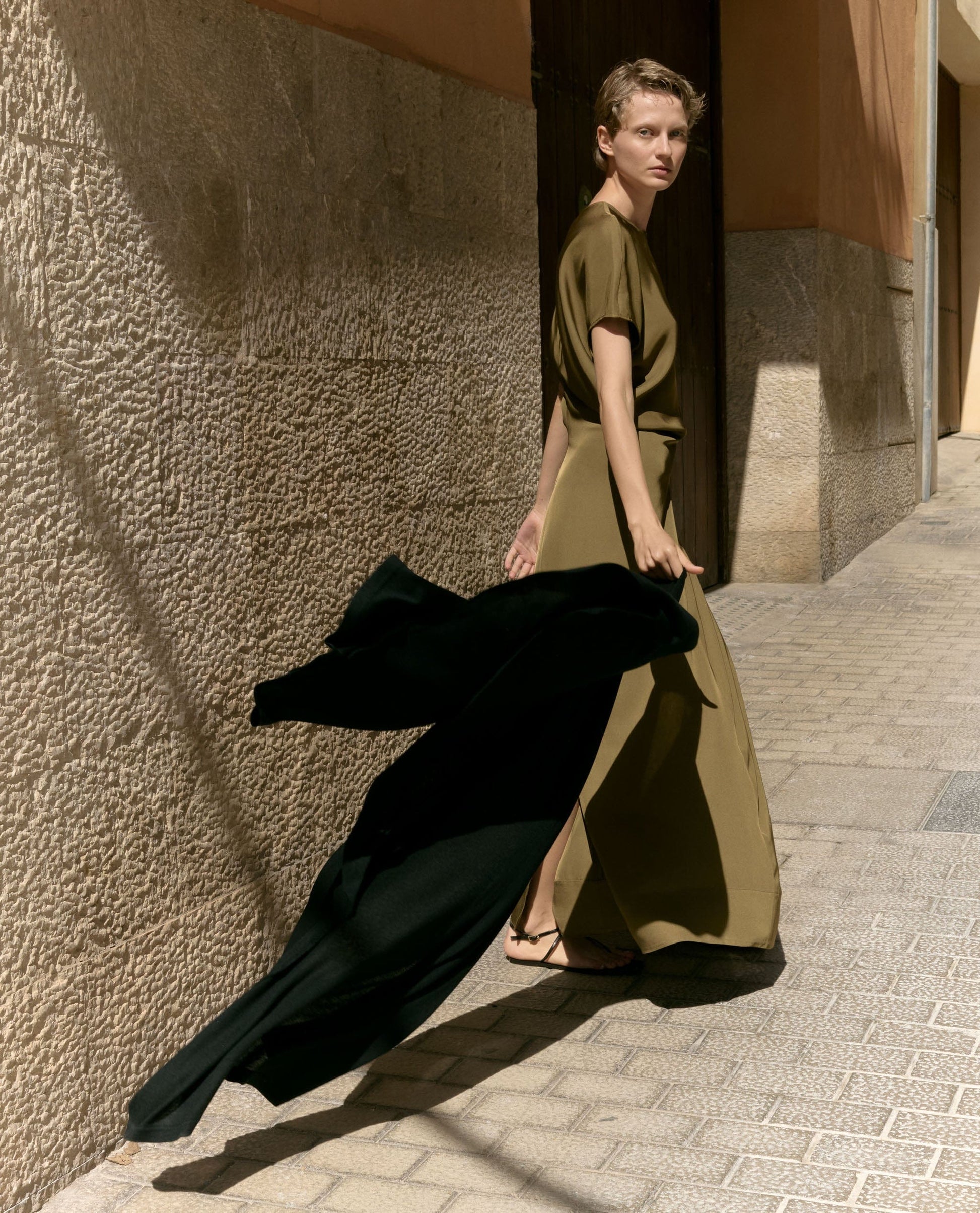 Image 5 of 5 showing woman holding Rise & Fall's black oversized cashmere scarf behind her as she walks.