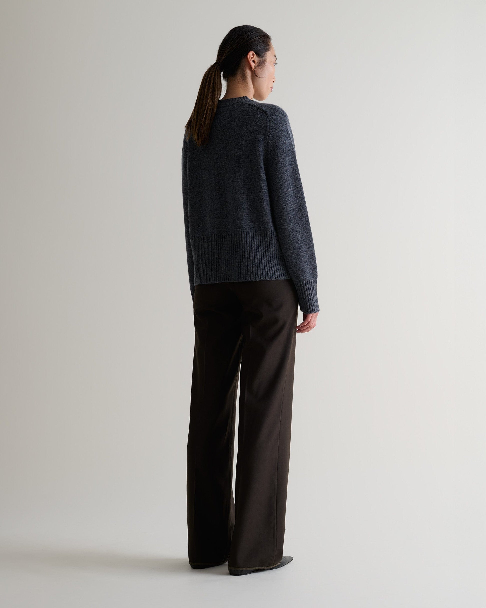 Image 5 of 5 showing back of woman wearing Rise & Fall graphite cashmere merino saddle sleeve crew neck jumper with chocolate silk trousers.
