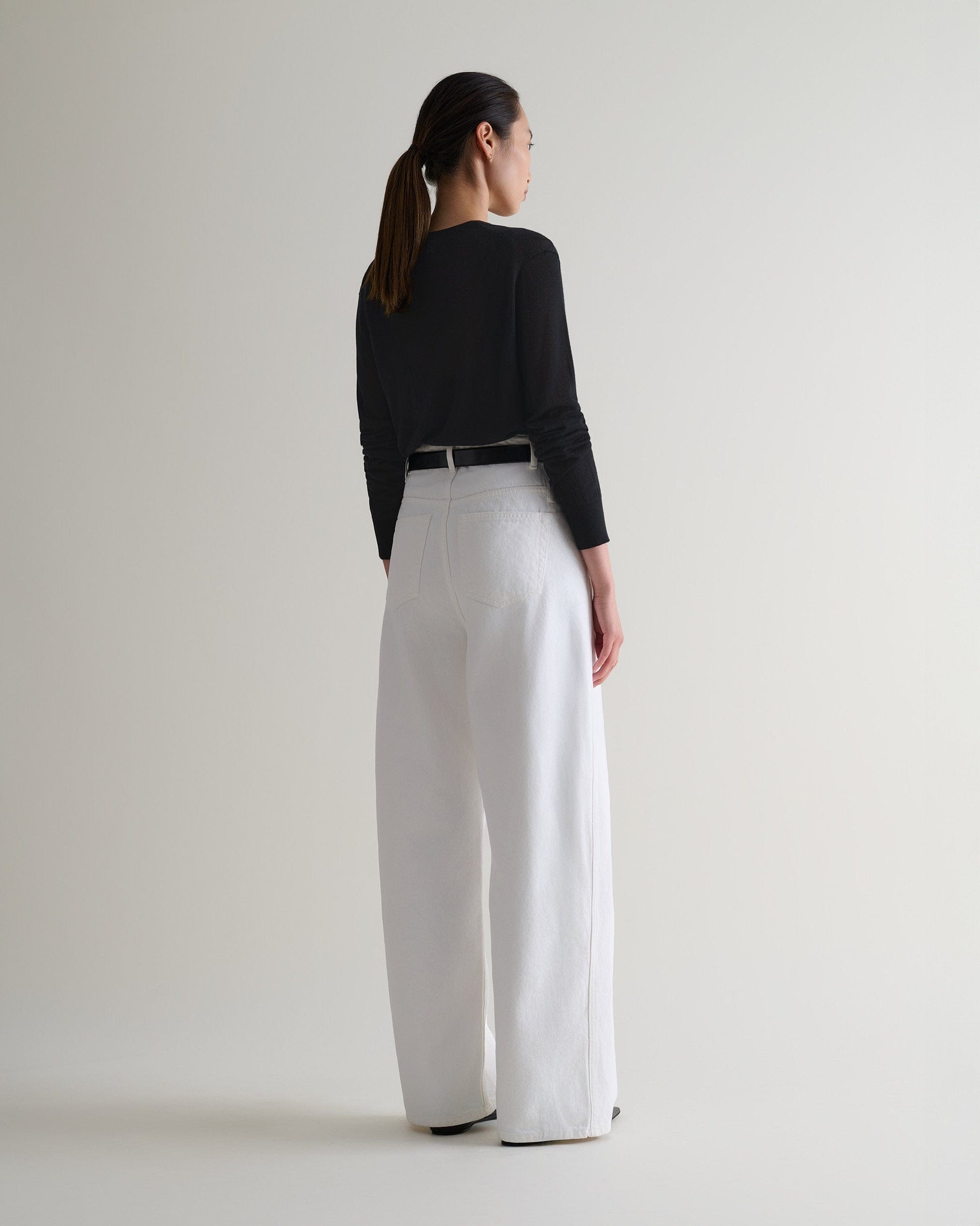 Image 5 of 5 showing back view of woman wearing Rise & Fall's black tencel cashmere double layered crew neck jumper with white jeans, black belt.