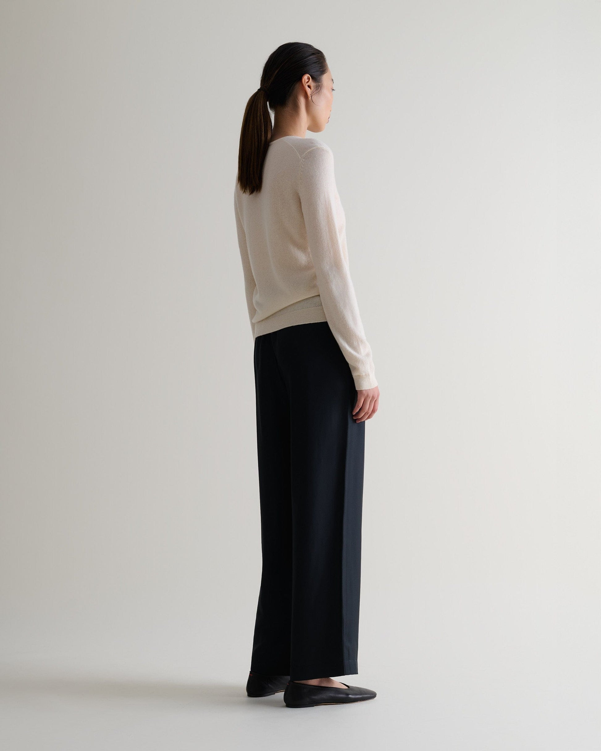 Image 5 of 5 showing side view of a woman wearing Rise & Fall's buttermilk cashmere merino henley jumper with black silk trousers. 
