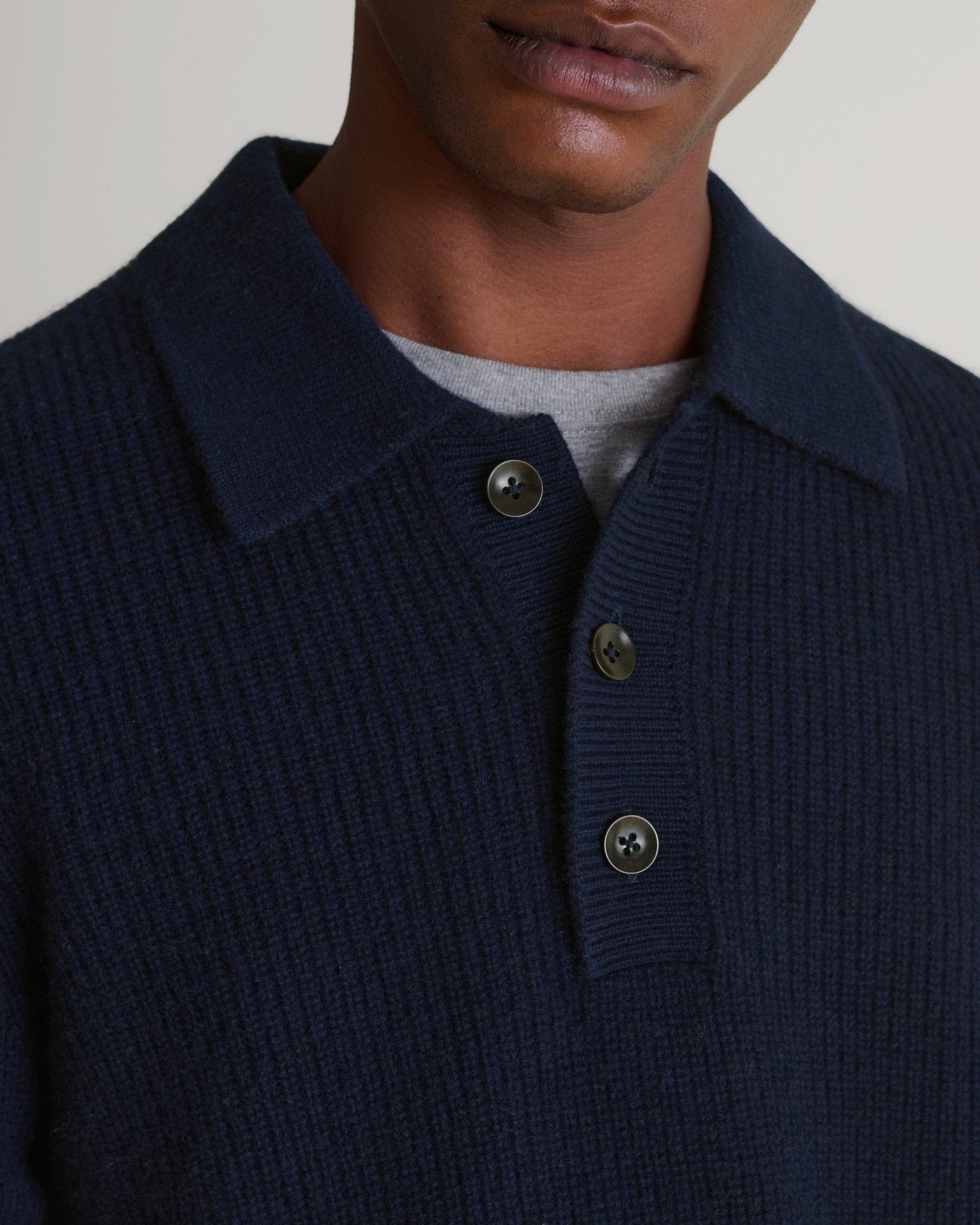 Image 5 of 6 showing close up of man wearing Rise & Fall's buttoned navy cashmere merino fisherman ribbed polo sweater. Worn with grey T-shirt undermeath.