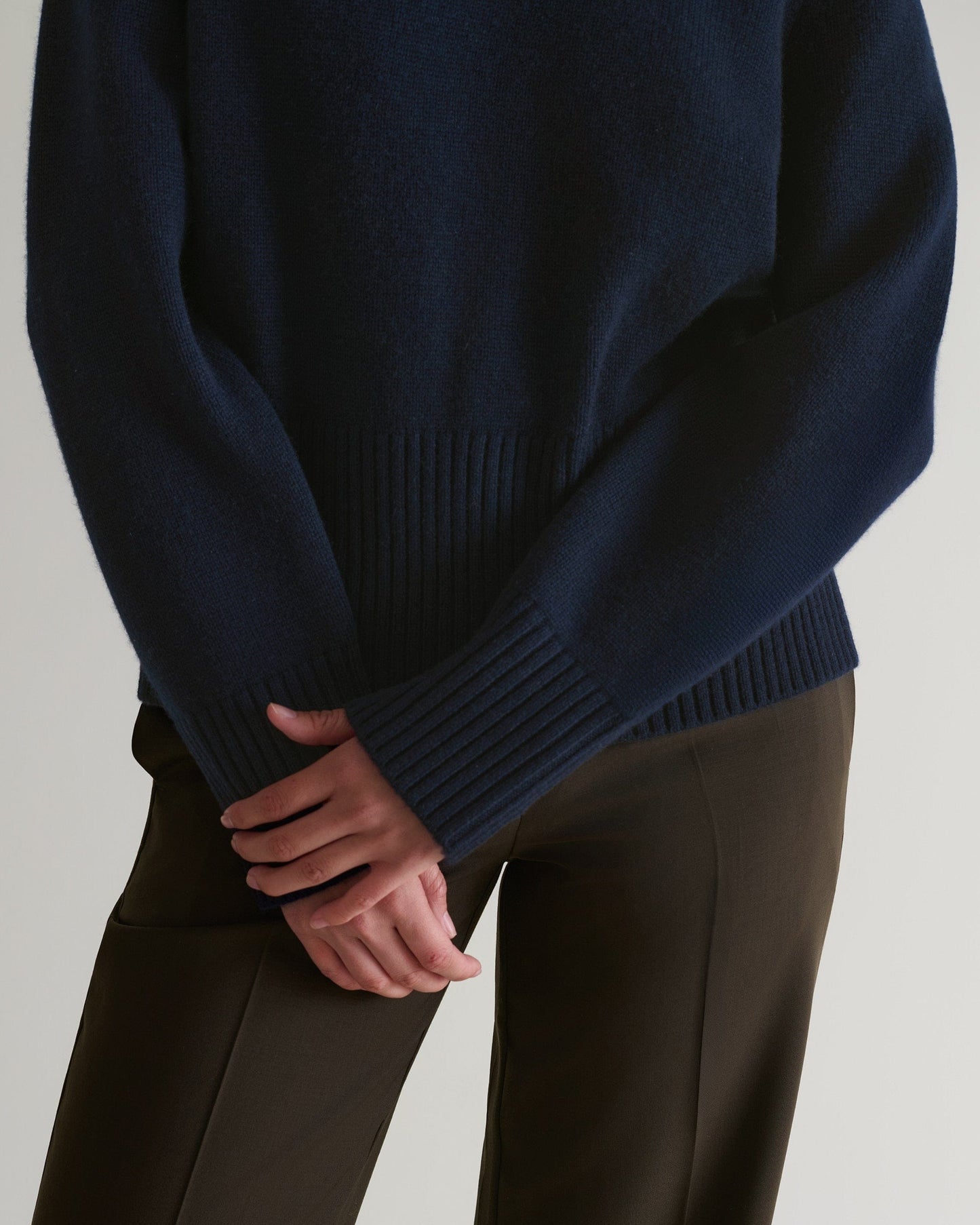 Image 6 of 6 showing close up of woman wearing Rise & Fall indigo cashmere merino saddle sleeve crew neck jumper with brown trousers.