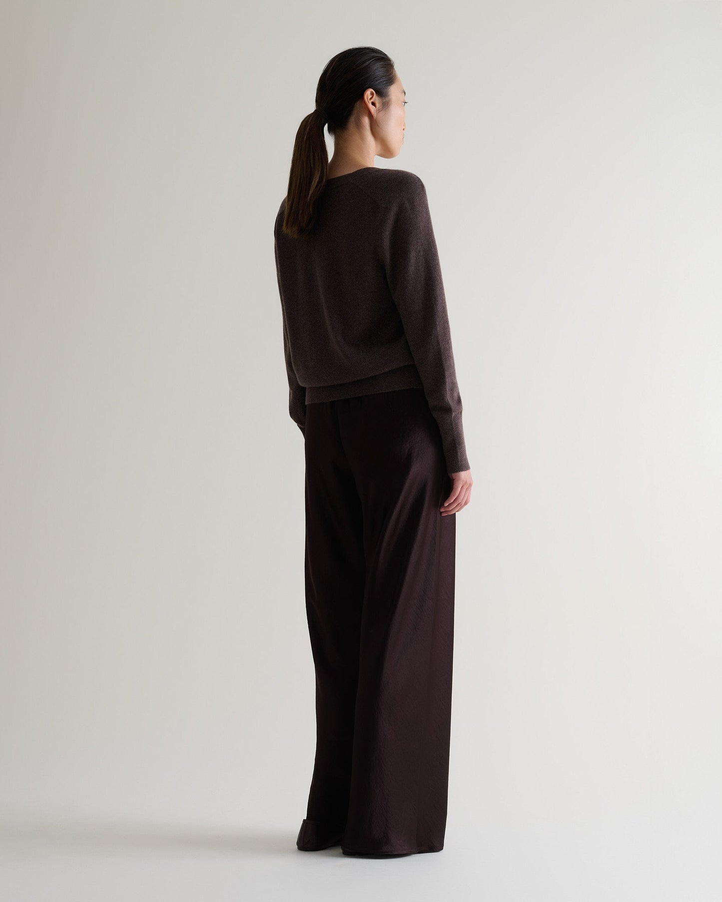 Image 6 of 6 showing back of woman wearing Rise & Fall's chocolate fine cashmere blouson cardigan with silk brown trousers.