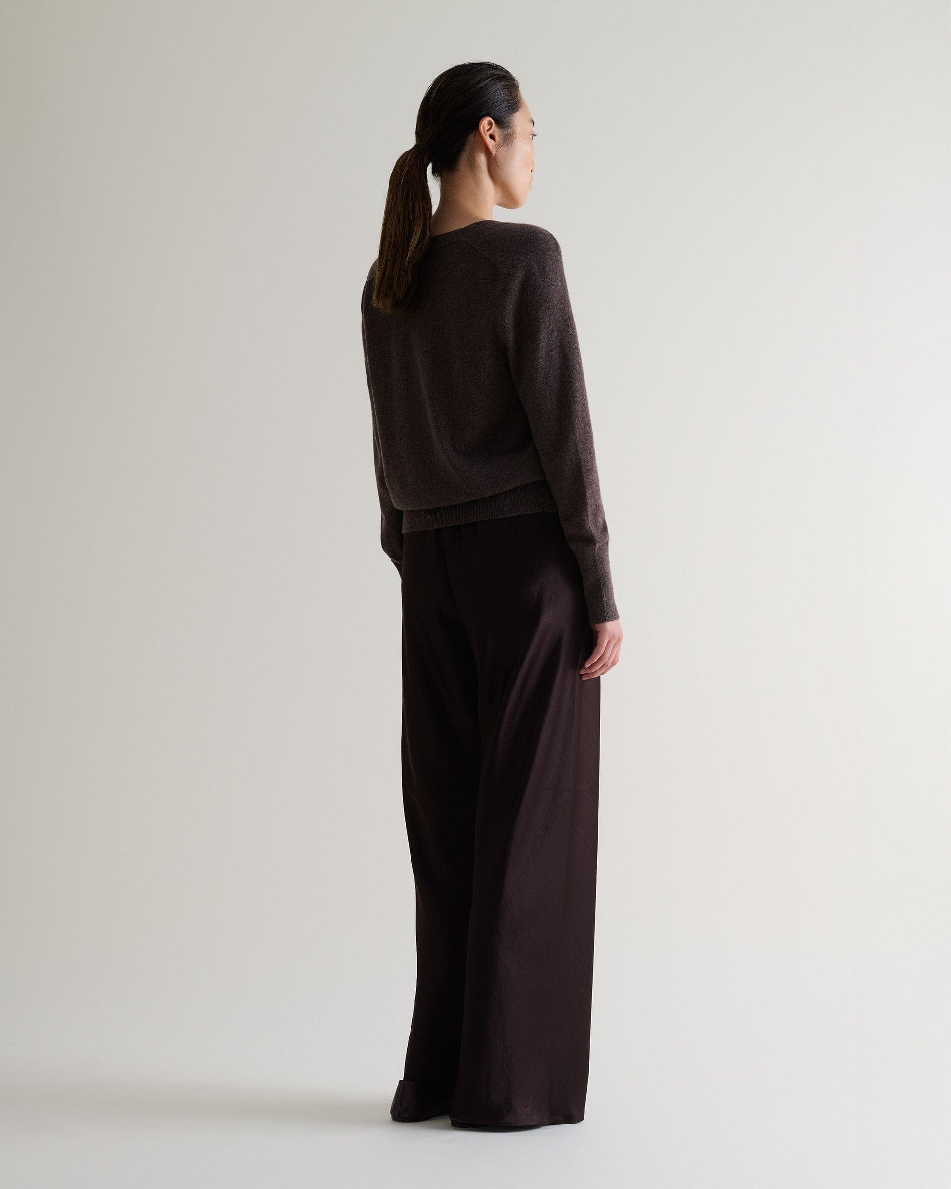 Image 6 of 6 showing back of woman wearing Rise & Fall's chocolate fine cashmere blouson cardigan with silk brown trousers.