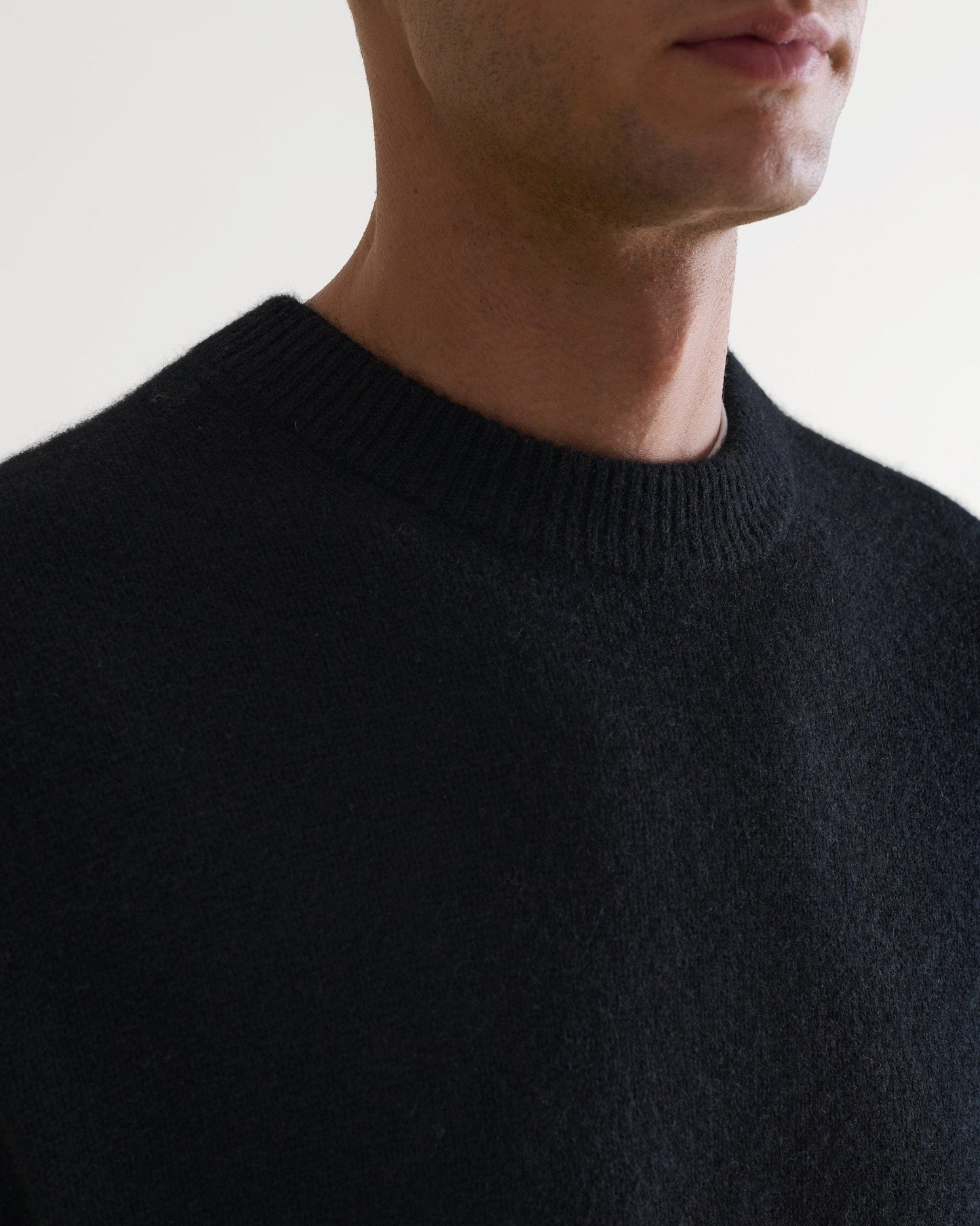 Image 6 of 7 showing close up of man wearing Rise & Fall's Finest Cashmere Mid-Weight Crew Neck Jumper in black.