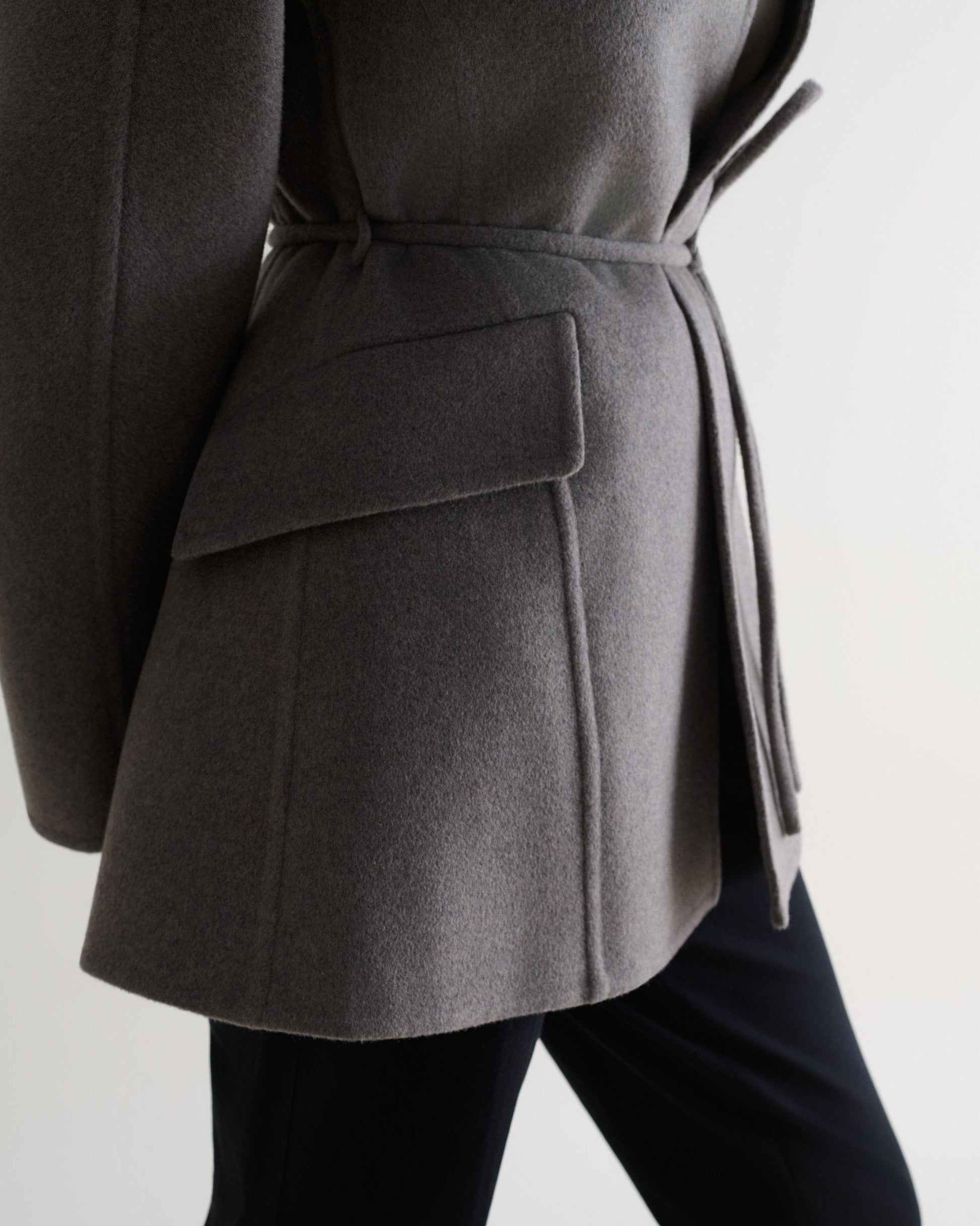 Image 6 of 7 showing close up side view of Rise & Fall's fawn cashmere wool double faced sculptural jacket with black trousers.