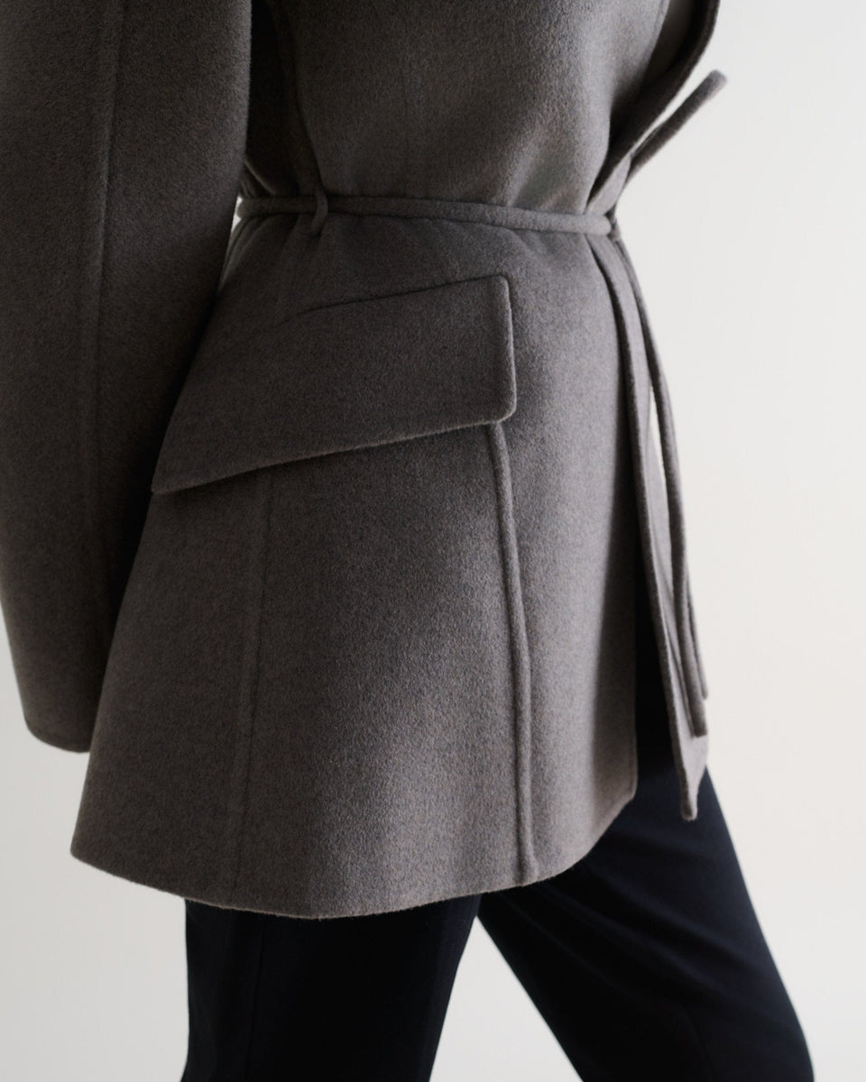 Image 6 of 7 showing close up side view of Rise & Fall's fawn cashmere wool double faced sculptural jacket with black trousers.