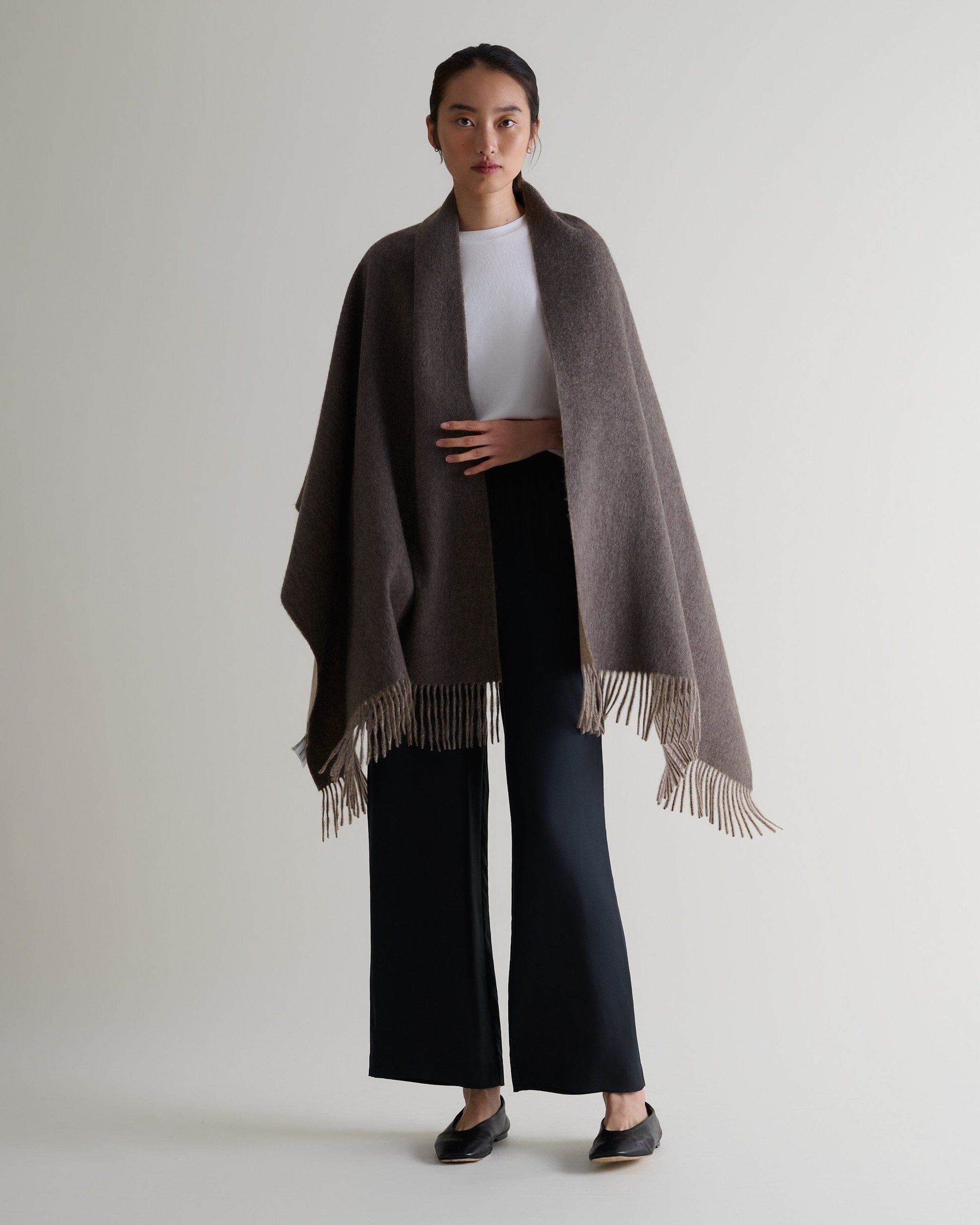 Image 6 of 7 showing woman wearing Rise & Fall's finest cashmere double faced wrap mole side with white T-shirt and black trousers.