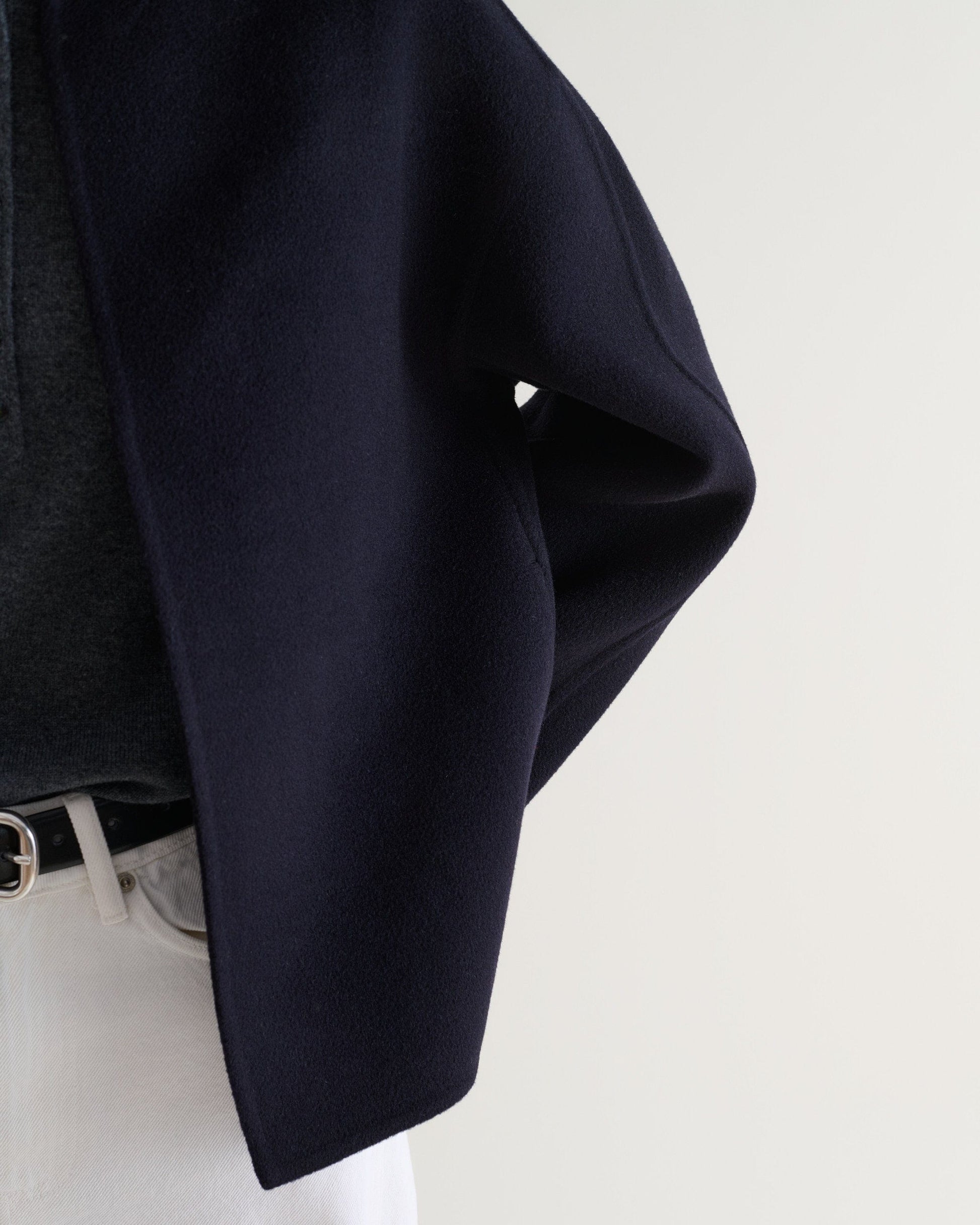 Image 7 of 7 showing a close up of Rise & Fall's navy cashmere wool double faced scarf jacket with white jeans.