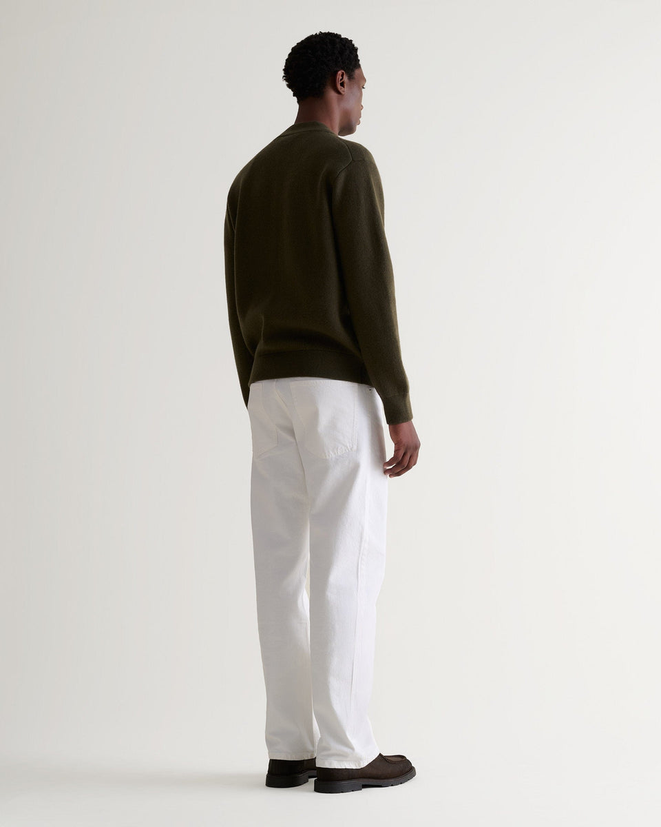 Man wears dark green cashmere merino double-faced knitted bomber with white trousers and brown shoes.