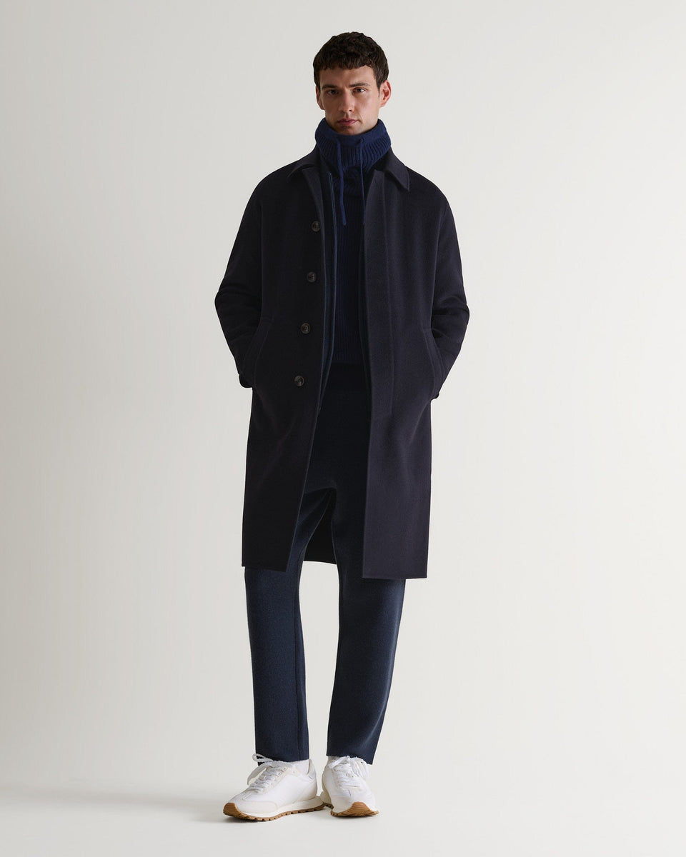 Full portrait view of man wearing indigo cashmere merino drawstring snood with navy overcoat and trousers