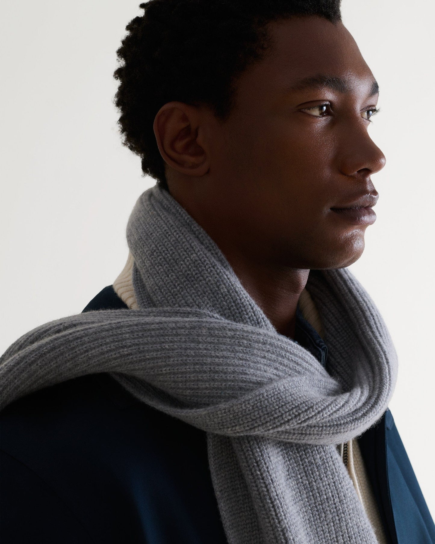 Close up of man wearing medium grey cashmere merino ribbed scarf with cream jumper and blue overcoat