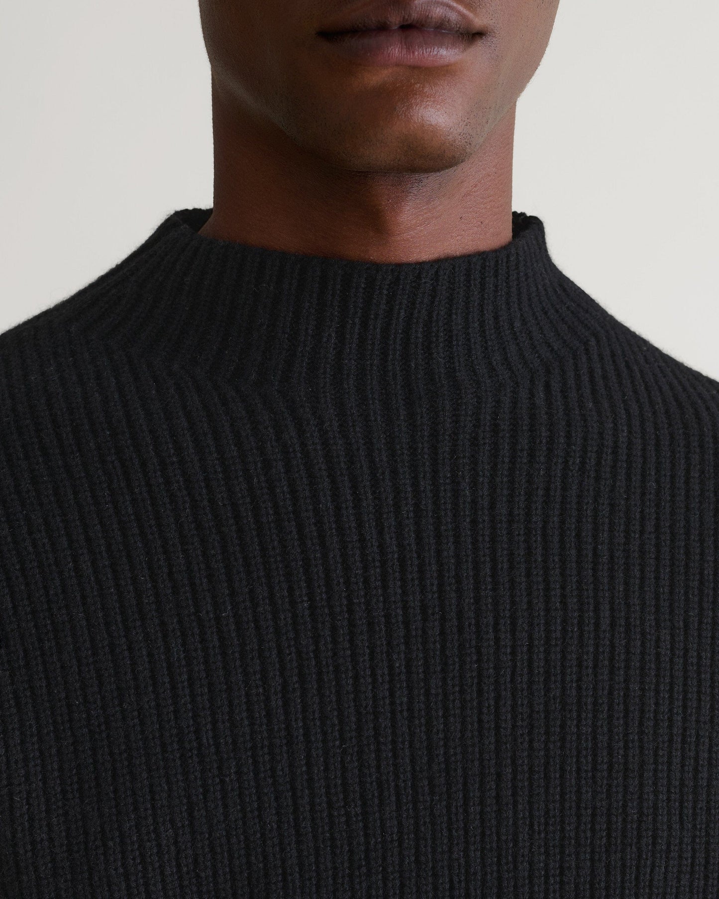 Man wearing Rise & Fall's black cashmere merino stand neck ribbed sweater. Close up of neckline.