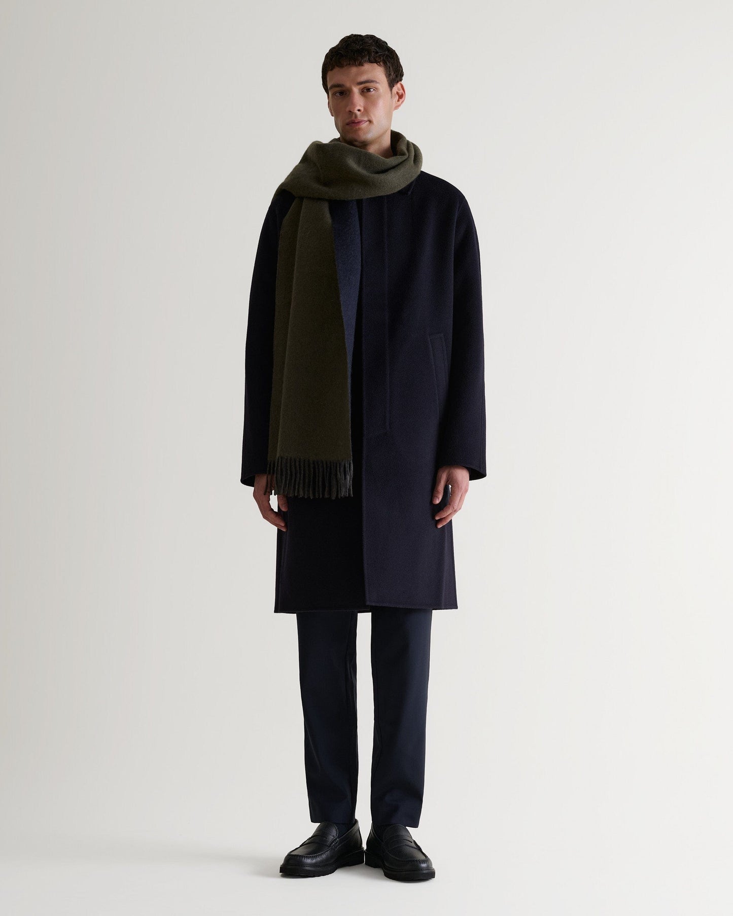 Full length view of man wearing Rise & Fall's finest cashmere double faced scarf - navy and olive. Worn with navy wool coat.