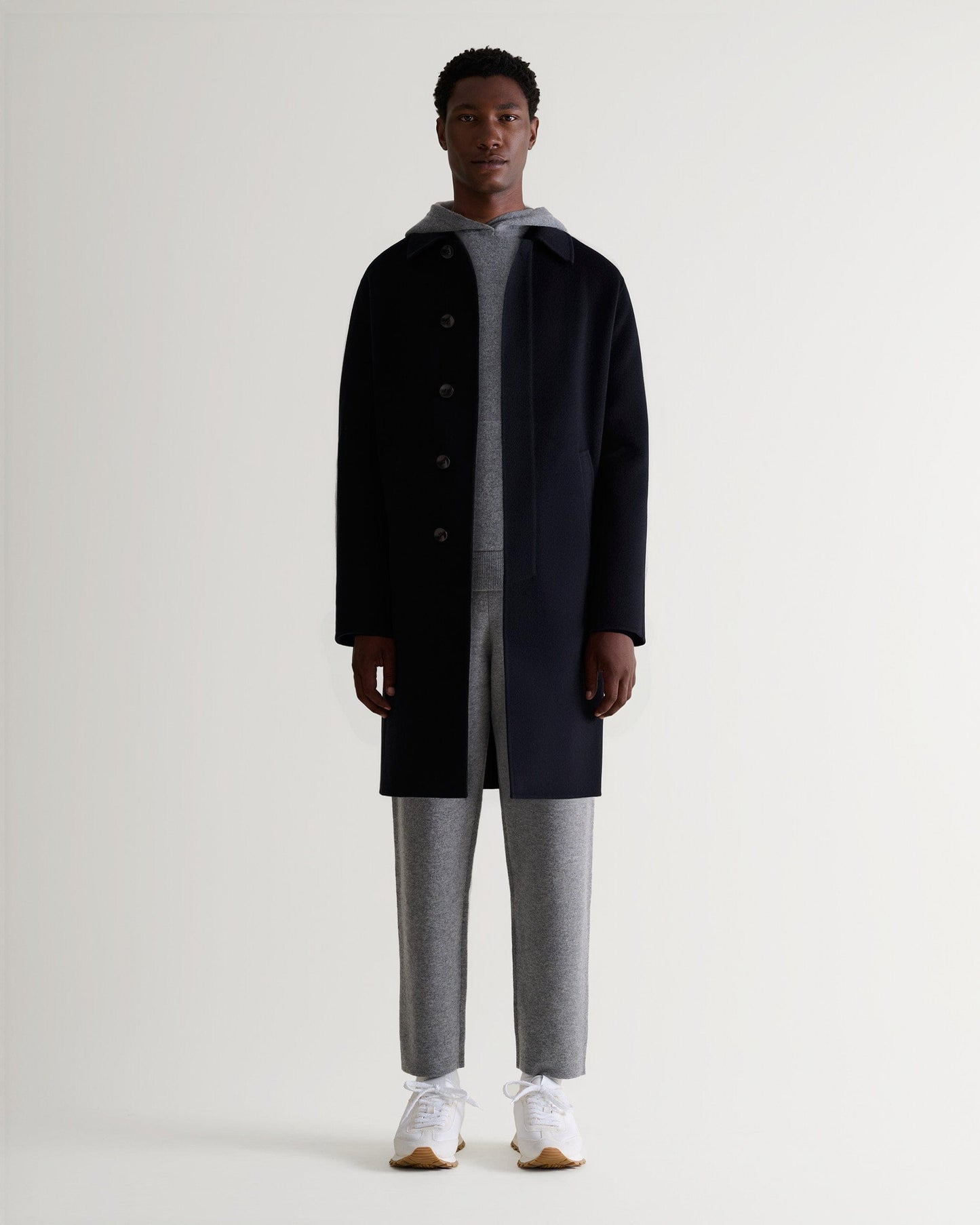 Full front view of man wearing Rise & Fall's grey cashmere merino double-faced hoodie and joggers with black wool coat.