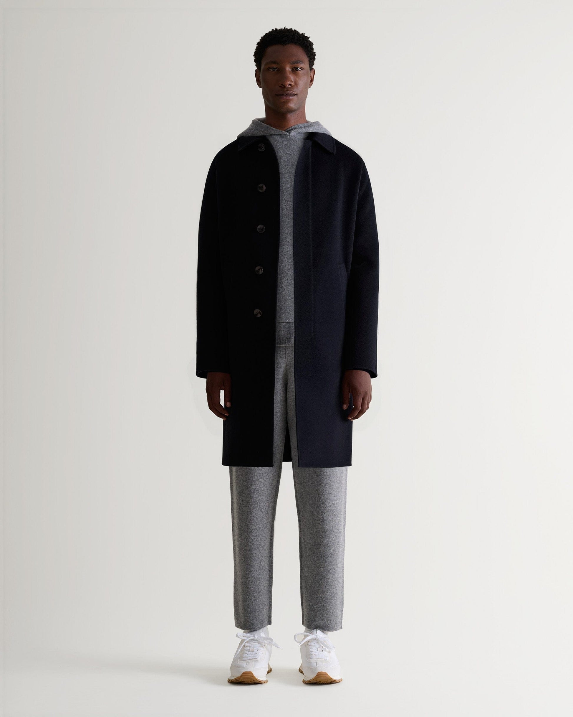 Full front view of man wearing Rise & Fall's grey cashmere merino double-faced hoodie and joggers with black wool coat.