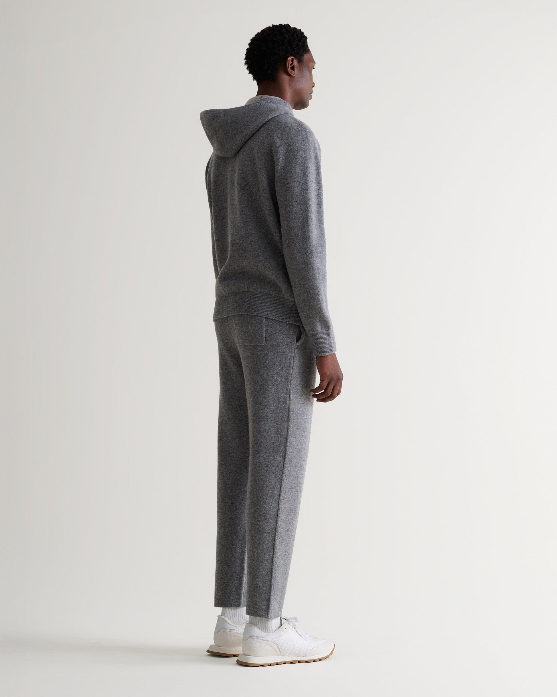 Full length side view of man wearing Rise & Fall's grey cashmere merino double-faced hoodie and matching joggers.