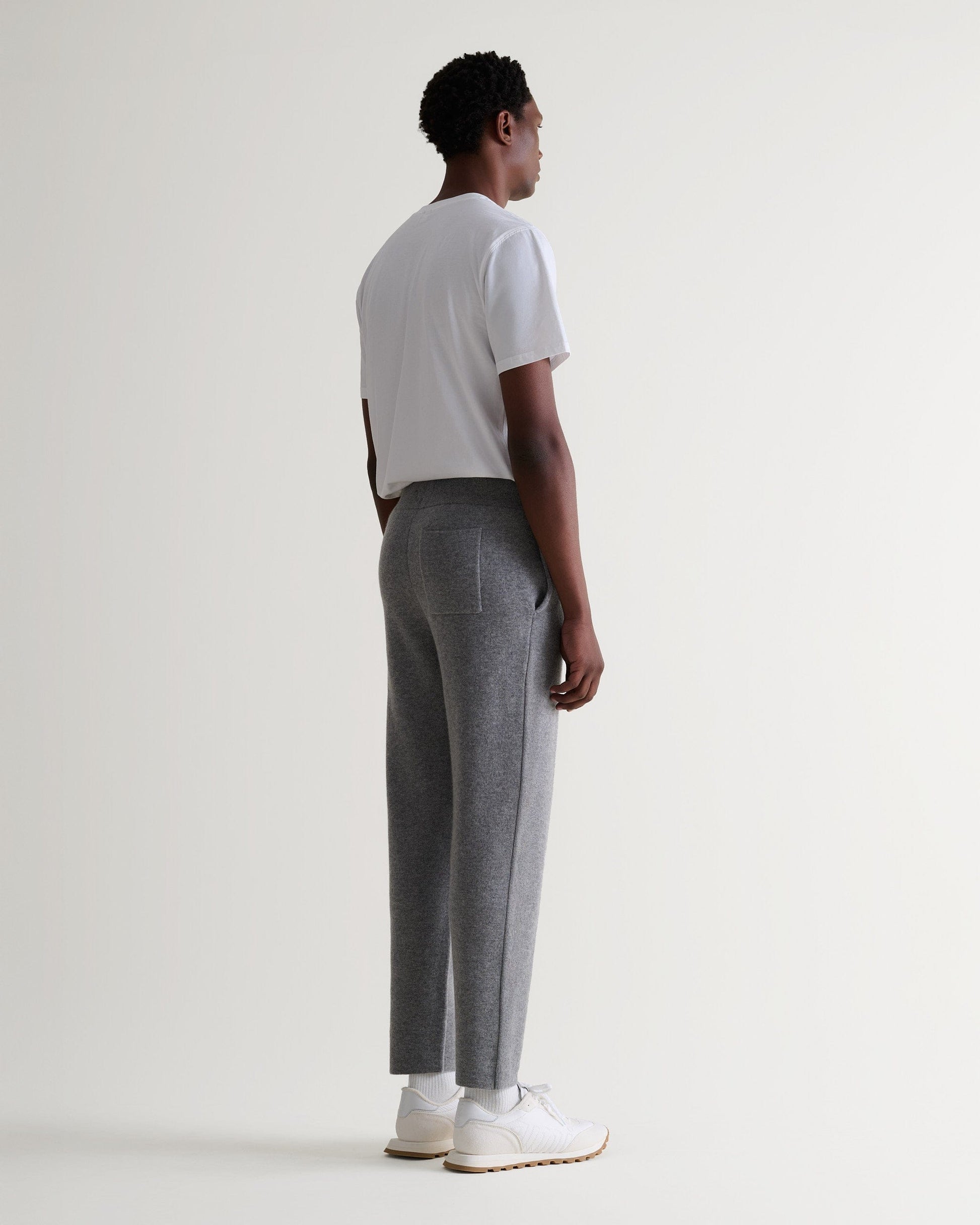 Side view of man wearing Rise & Fall's grey cashmere merino double-faced joggers with white crew neck T-shirt and trainers.