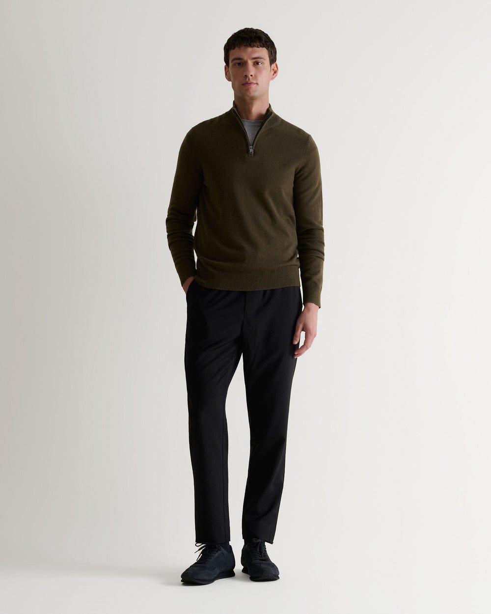 Full length front view of man wearing Rise & Fall's military green finest cashmere 1/4 zip jumper. Worn with black trousers.