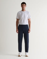 Full length front view of man wearing Rise & Fall's navy cashmere merino double-faced joggers with white T-shirt and trainers. 