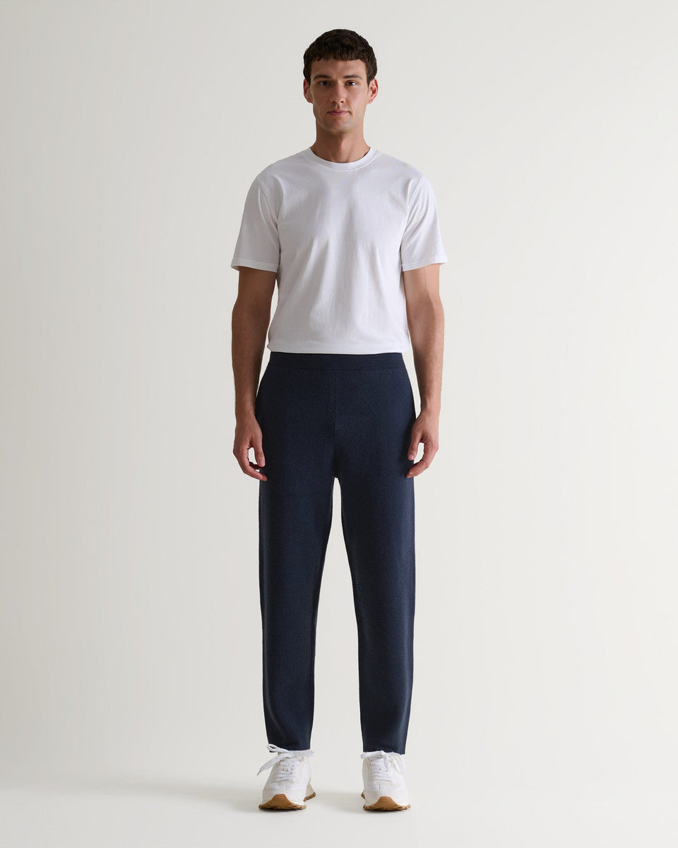 Full length front view of man wearing Rise & Fall's navy cashmere merino double-faced joggers with white T-shirt and trainers. 