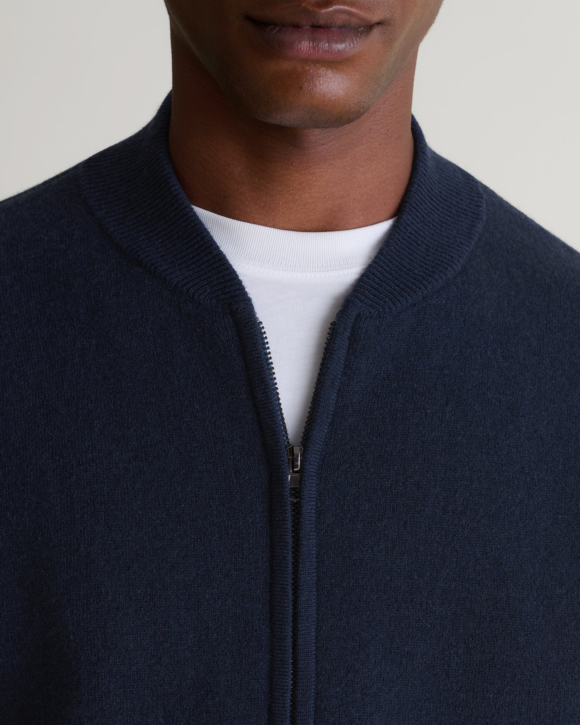 Close up of man wearing Rise & Fall's navy cashmere merino double-faced knitted bomber jacket with a white T-shirt.