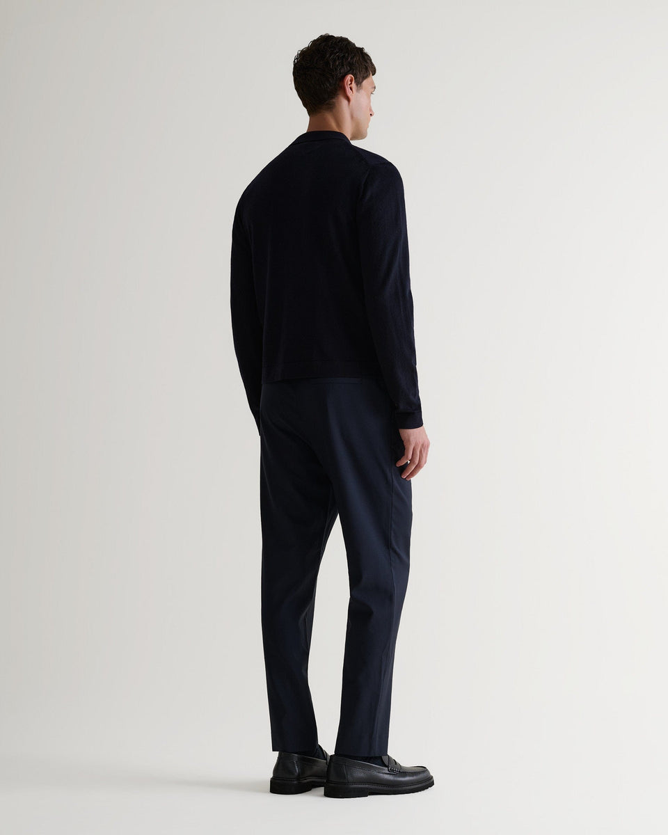 Full length back view of man wearing Rise & Fall's navy fine merino knit shirt. Worn with navy trousers and black shoes. 