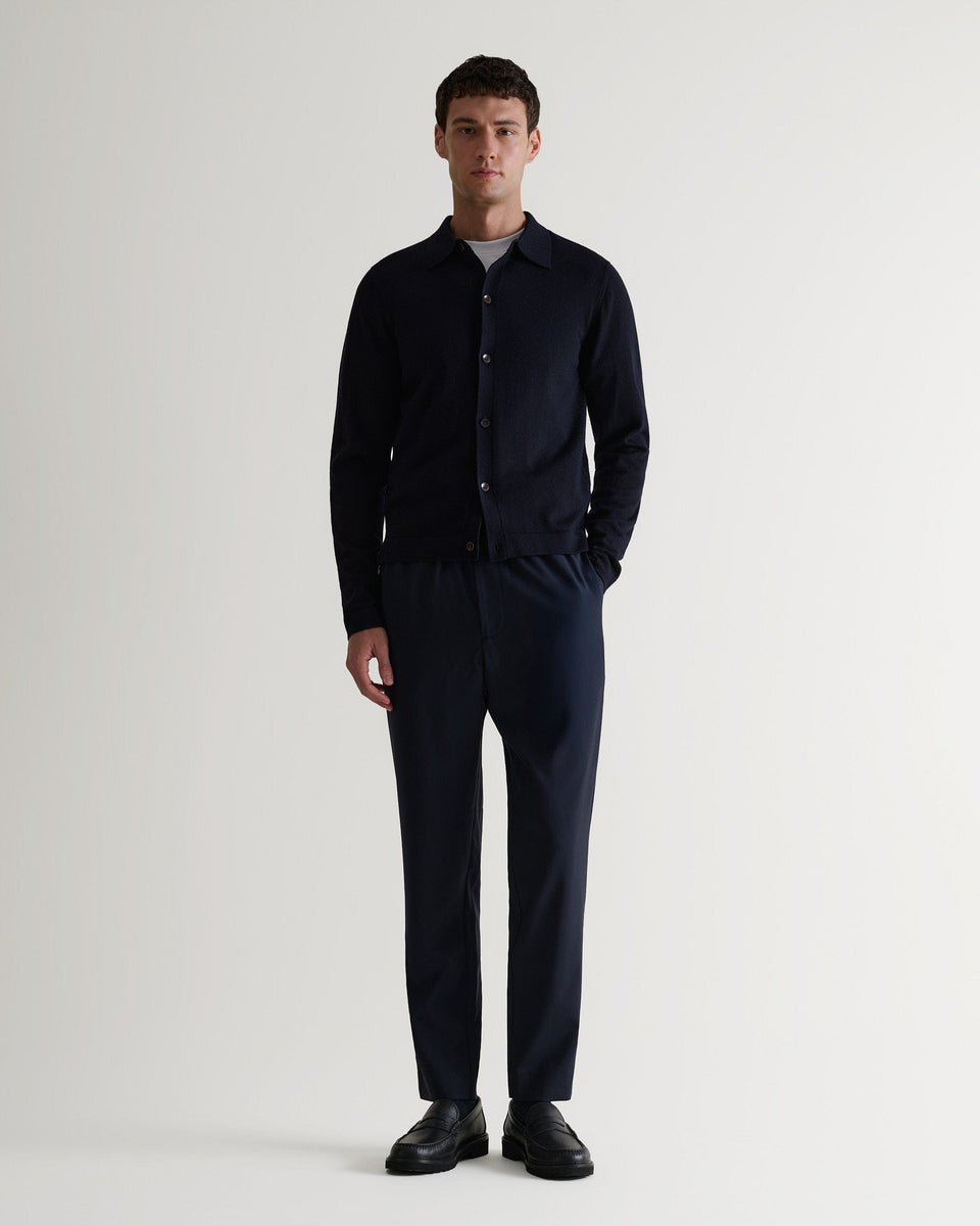 Full length front view of man wearing Rise & Fall's navy fine merino knit shirt. Worn with navy trousers and black shoes. 