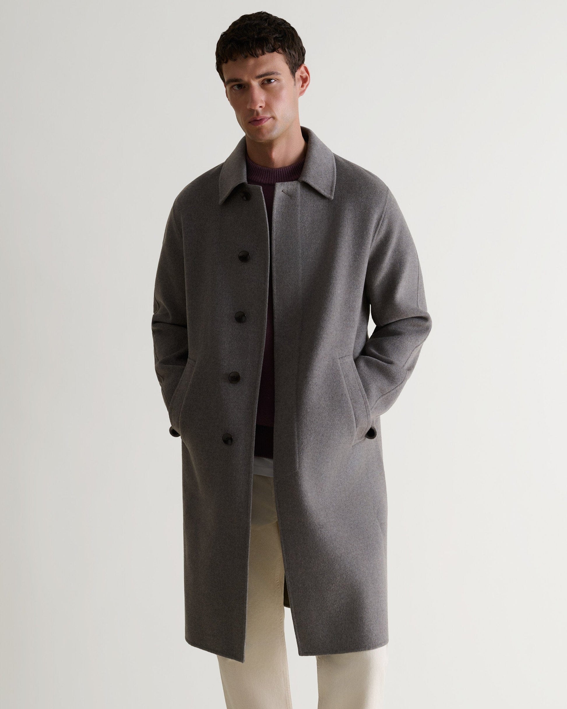 Man wears fawn cashmere merino double-faced wool coat. Paired with cream jeans and black jumper. Full length view.