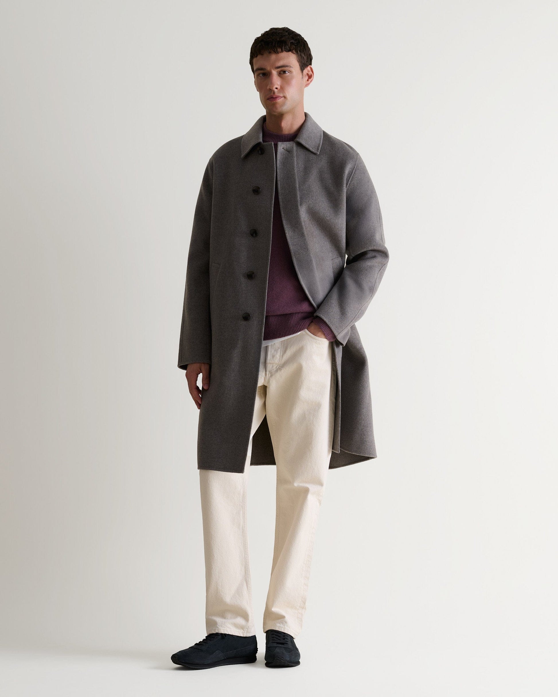 Full length front view of man wearing grey cashmere merino wool double-faced coat. Matched with burgundy jumper and cream jeans.